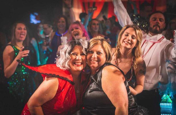 A group of party-goers dancing and celebrating at a nightclub with colorful lighting.