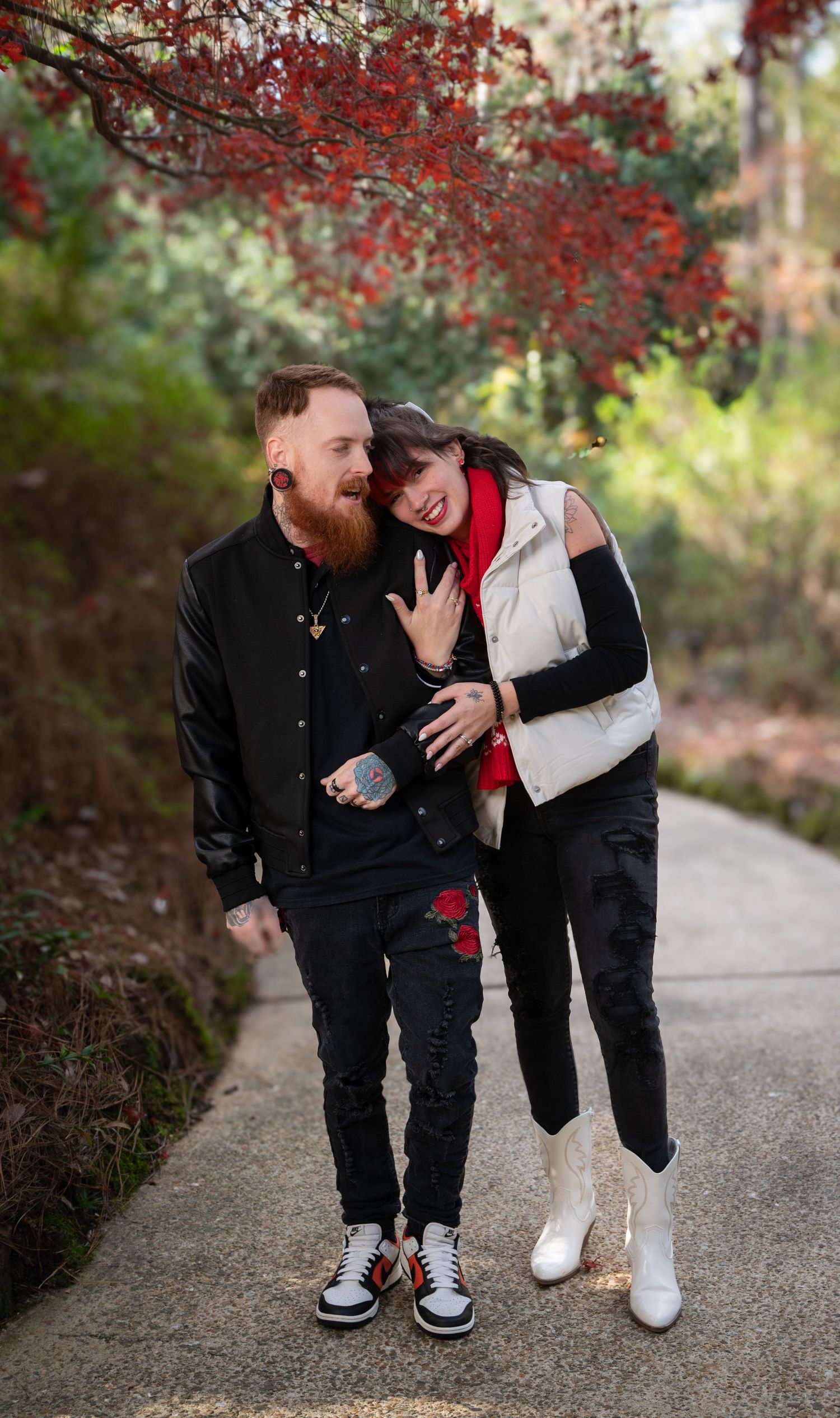 Couple sharing a joyful moment under red autumn foliage on a walking path.