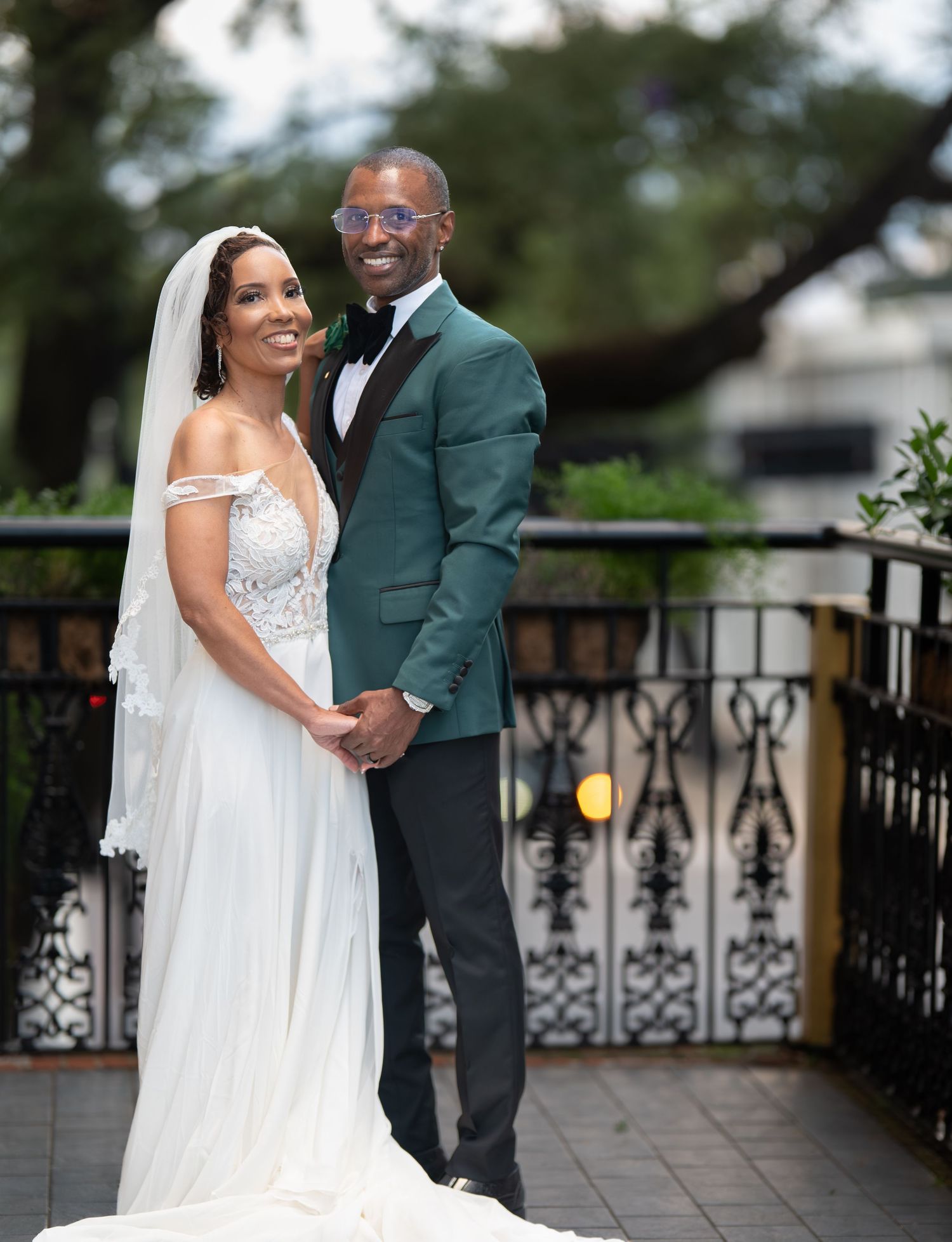 A couple shares an intimate moment on an outdoor terrace with decorative iron railings during their wedding celebration.