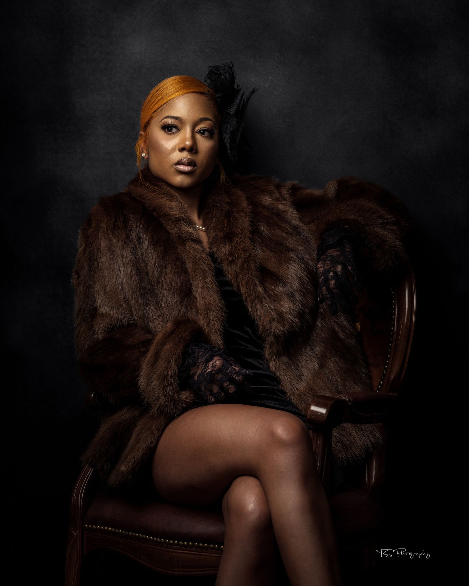 Portrait of woman in fur coat sitting on vintage chair against dark dramatic background.