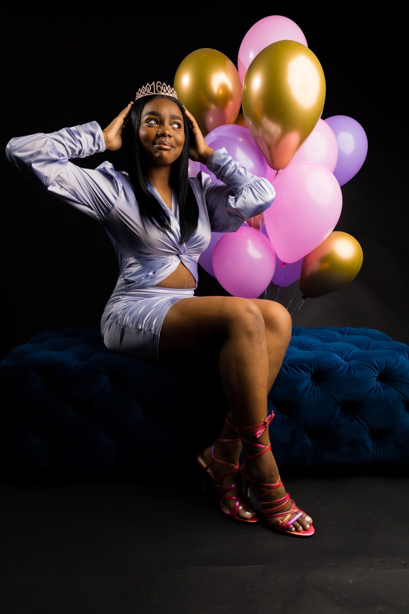 Glamorous portrait with gold and pink balloons against dark backdrop featuring a tiara and sparkly outfit.