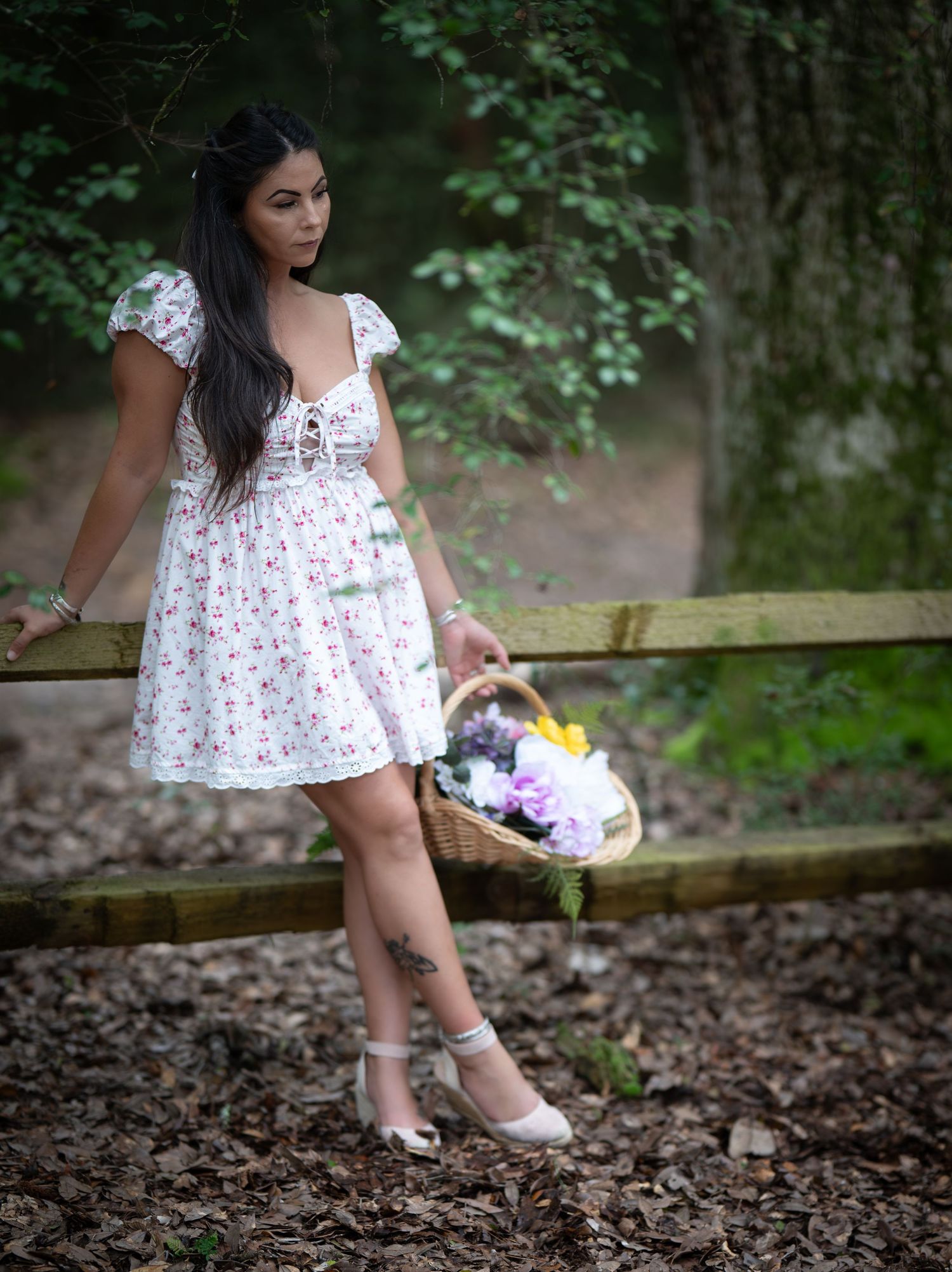 Cottage core fashion shoot featuring a floral summer dress and basket of flowers in a wooded setting.