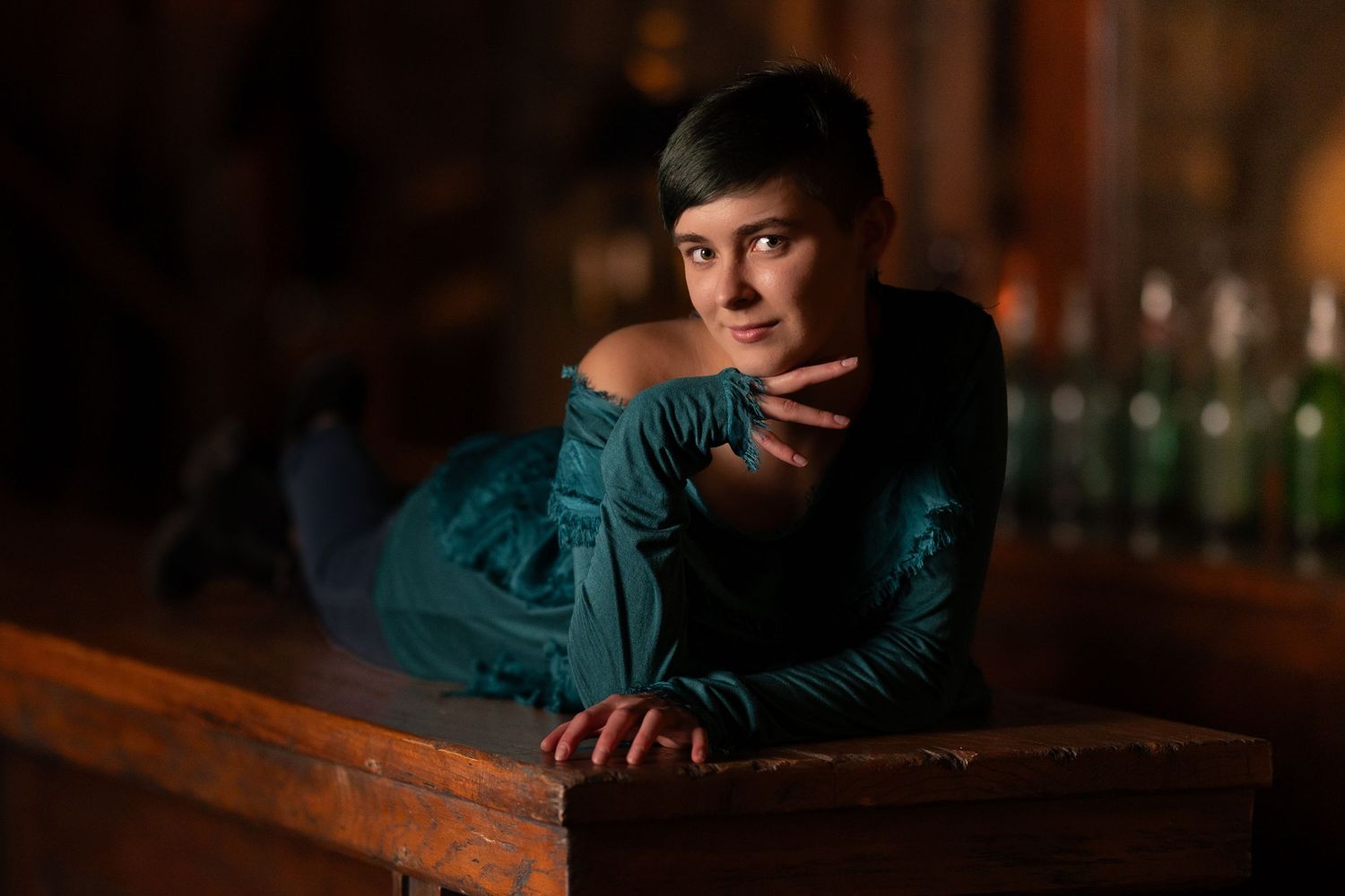 Low light portrait with dramatic orange lighting featuring person in teal jacket leaning on wooden surface.