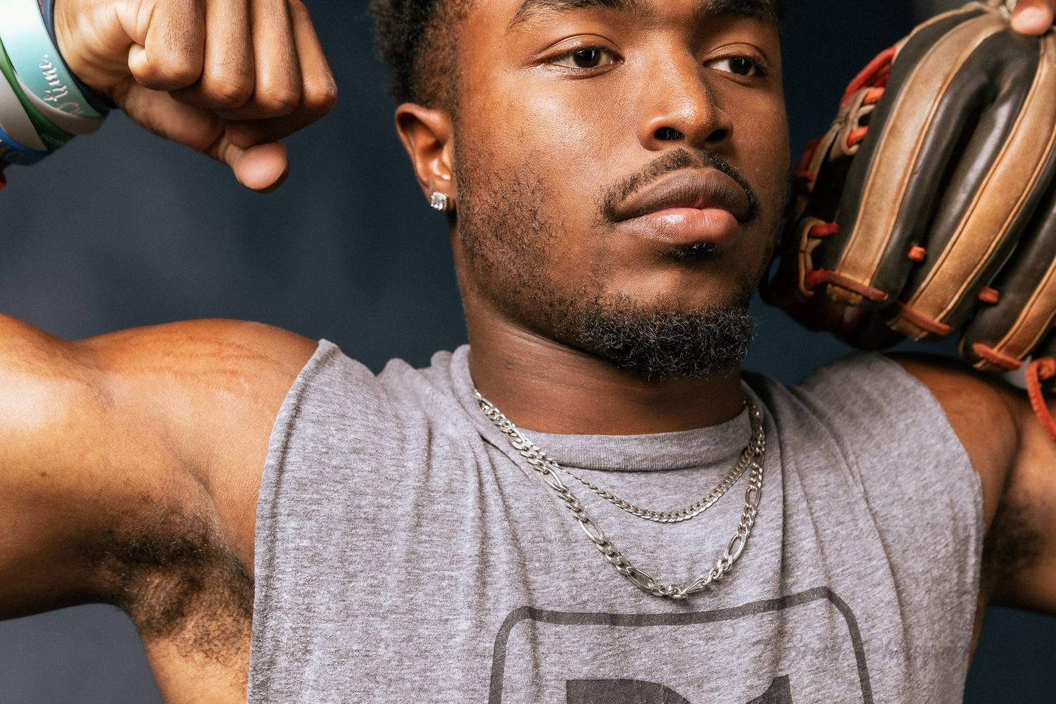 Athletic portrait showing a baseball glove and silver chain necklace against a dark background.