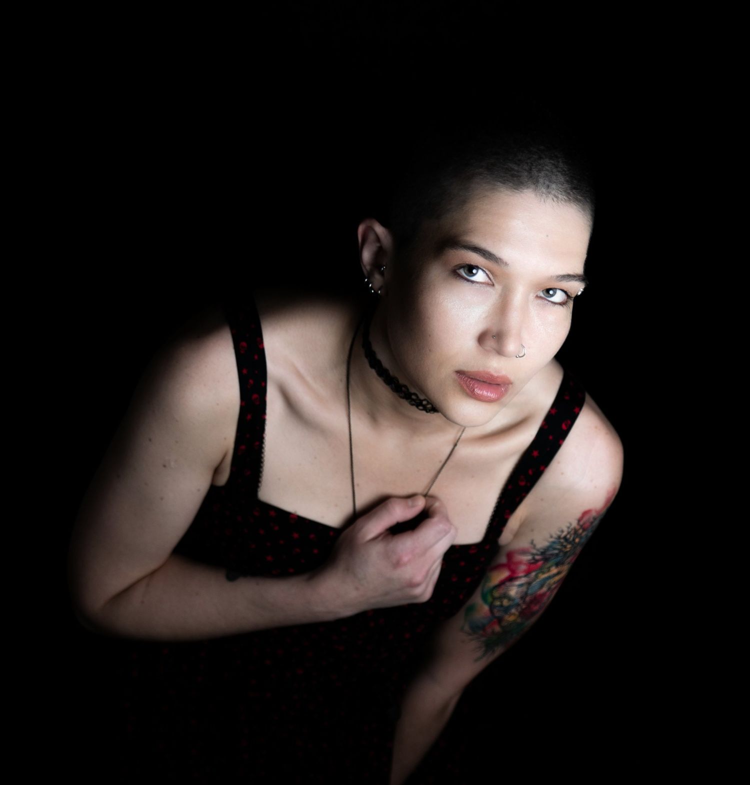 Dramatic portrait of a model in black against dark background with visible tattoo on shoulder.