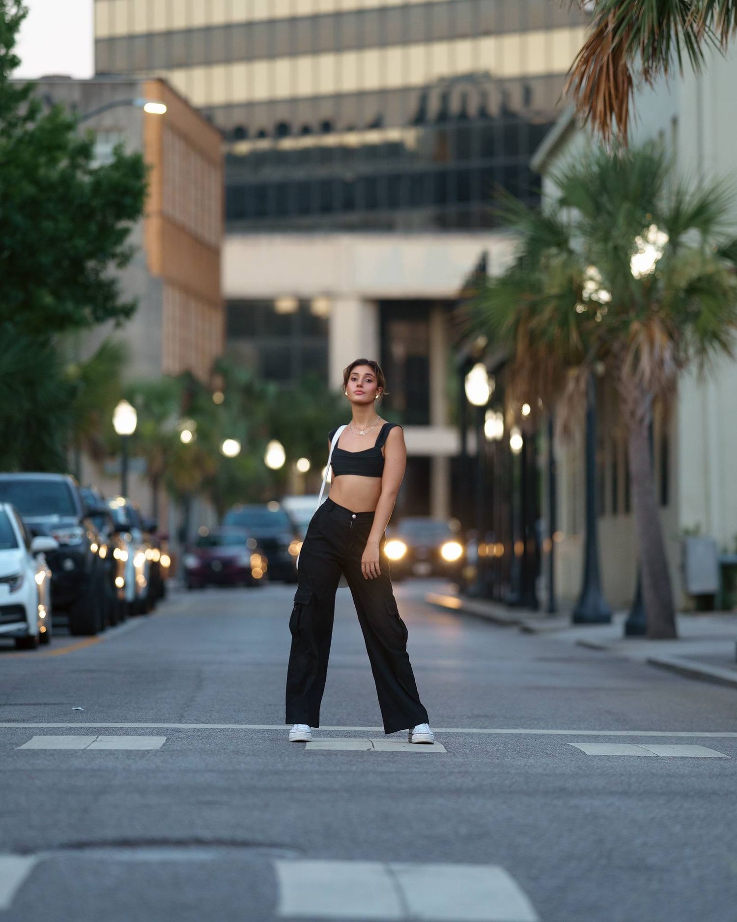 Stylish street fashion photo at dusk with city lights and palm trees in the background.