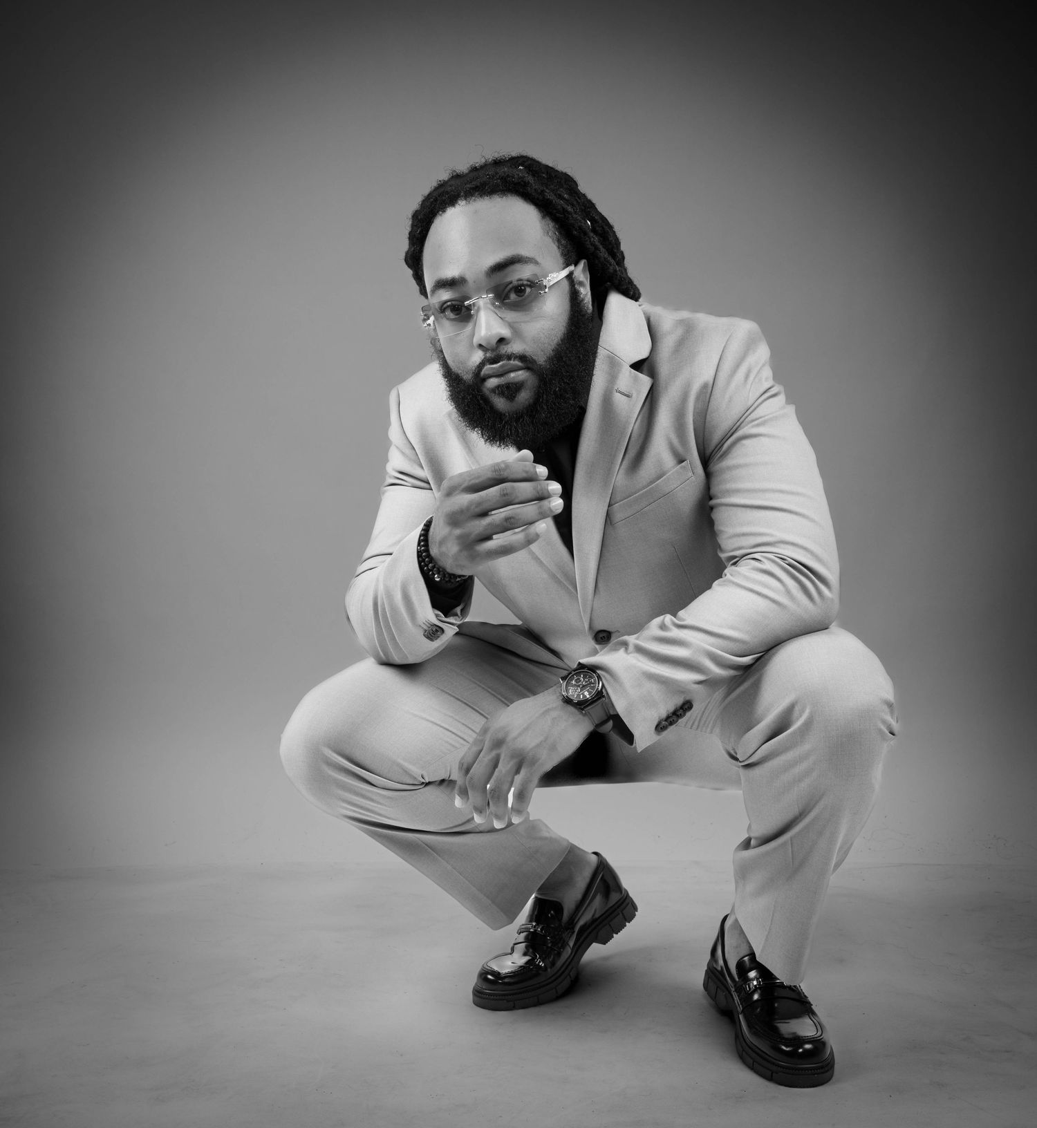 Three black and white photos show someone in a light-colored suit sitting low in dynamic poses against a plain background.