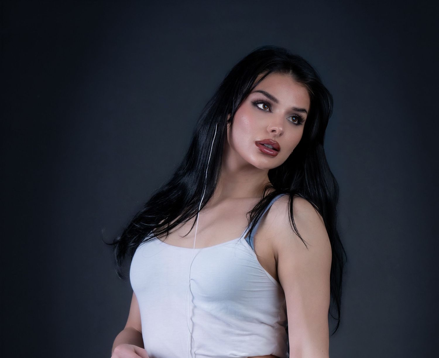 Portrait of a woman with dark hair wearing a white tank top against a dark background.
