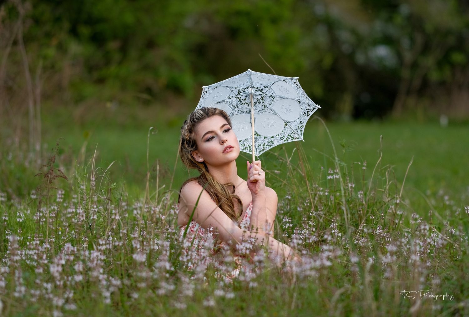 Person in floral field holding lace parasol in dreamy spring setting.