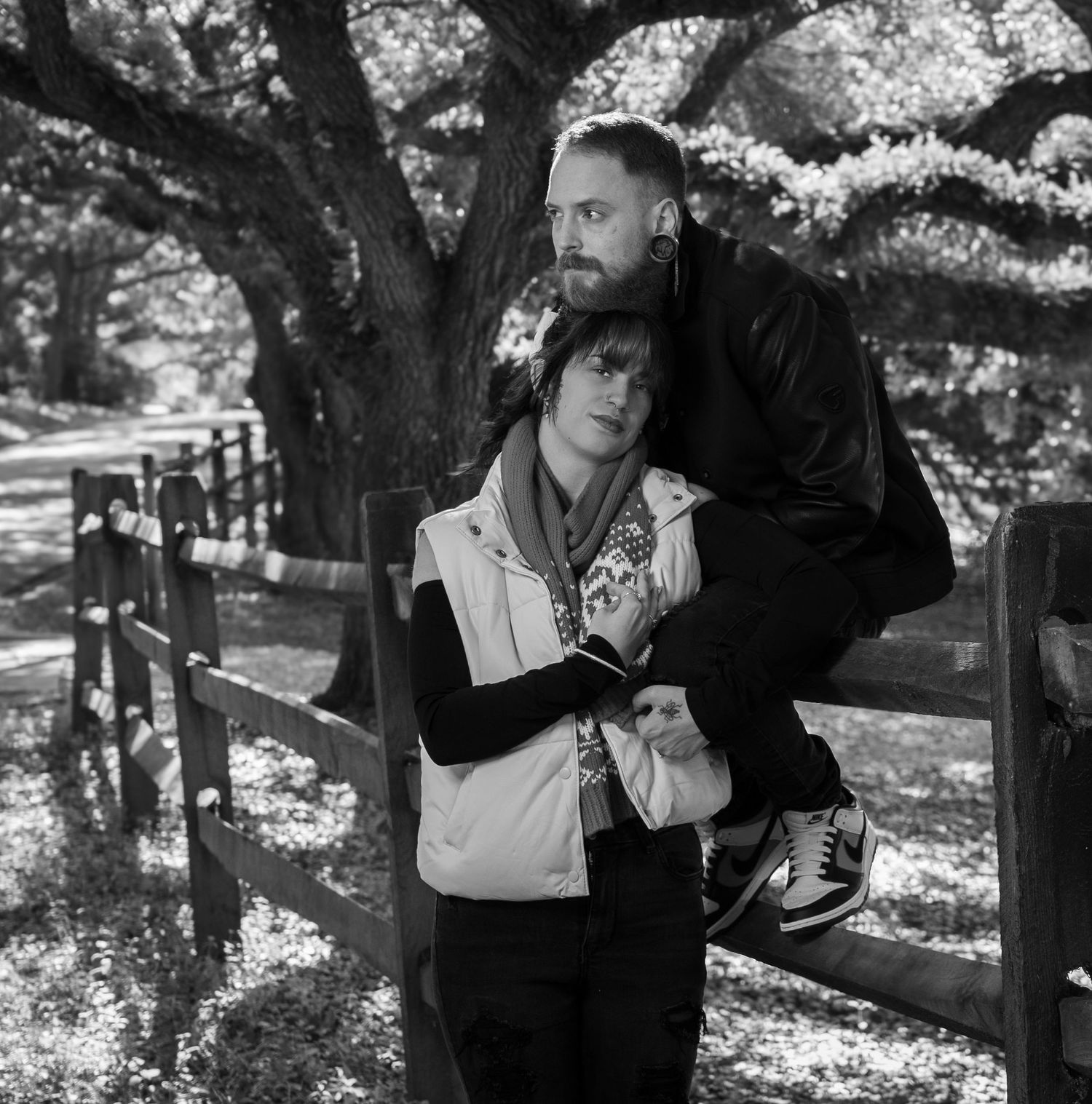 Black and white photo of couple embracing by a tree in a park setting.