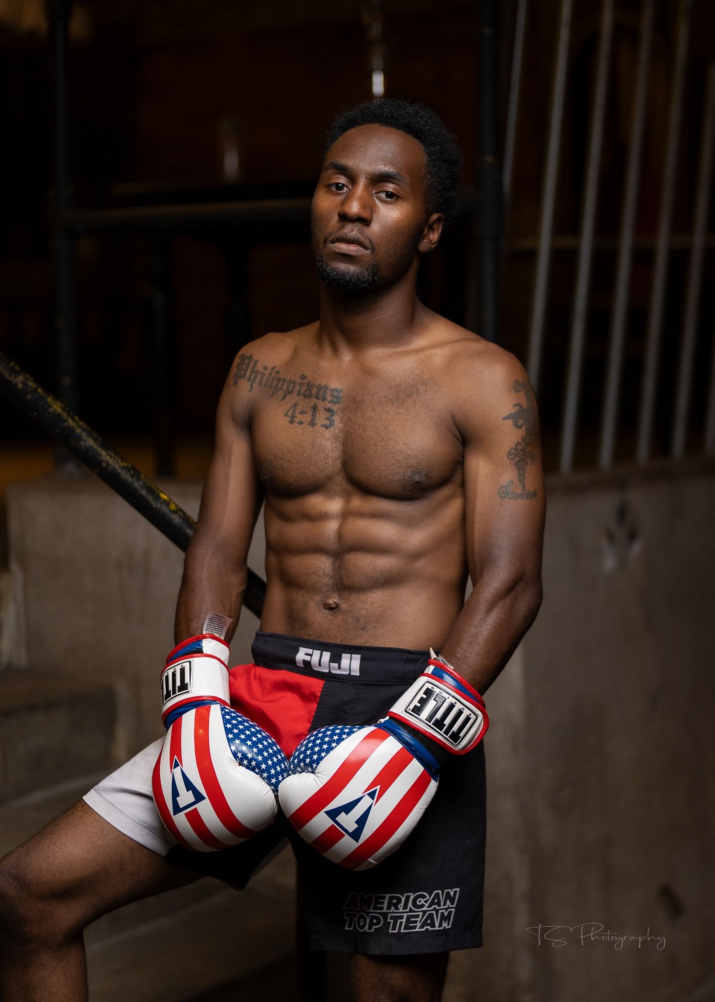 Athletic boxer in patriotic shorts showing muscular physique in dark gym setting.
