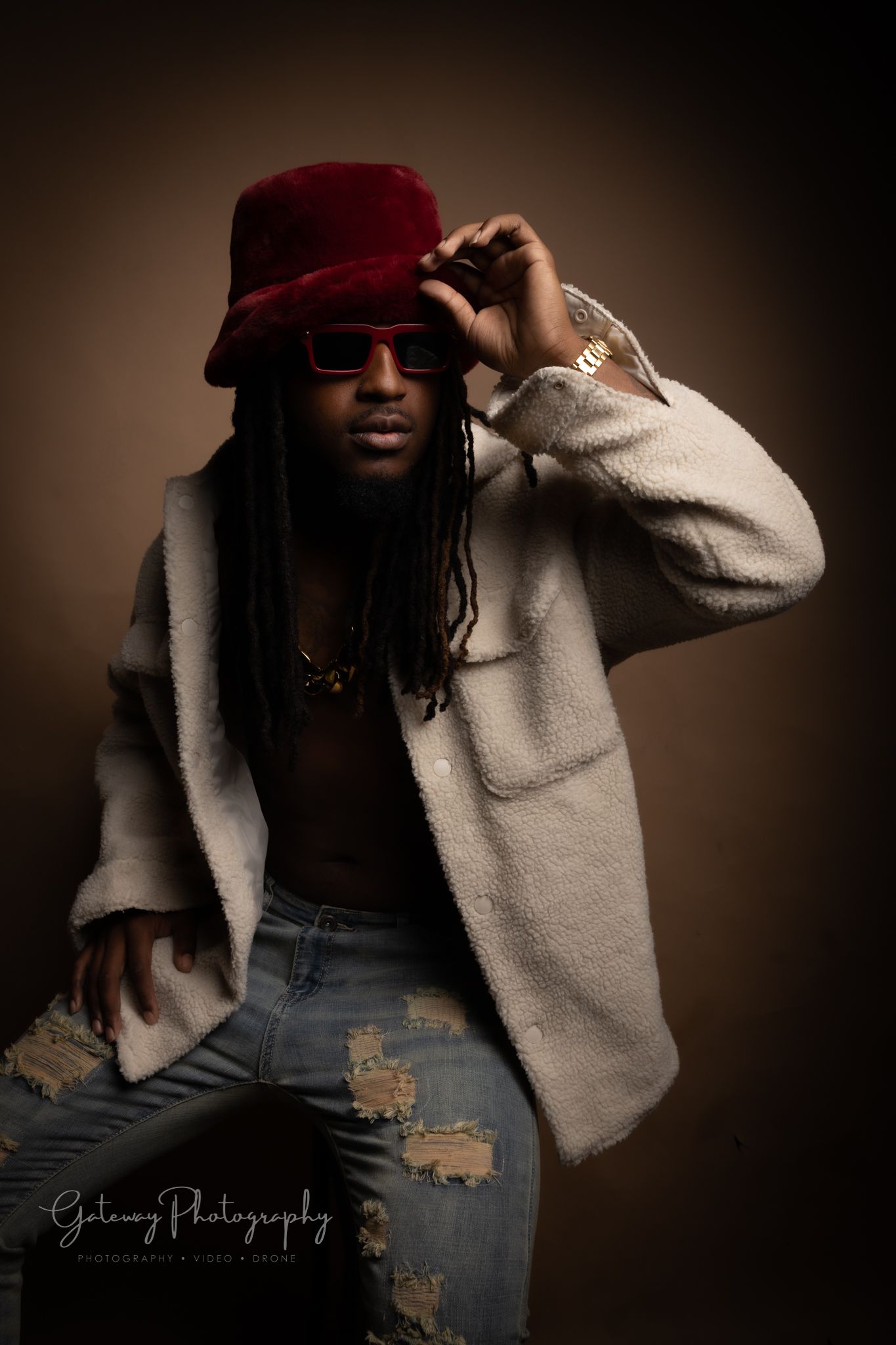 Stylish portrait with red fedora, white fuzzy coat and distressed jeans against moody brown backdrop.