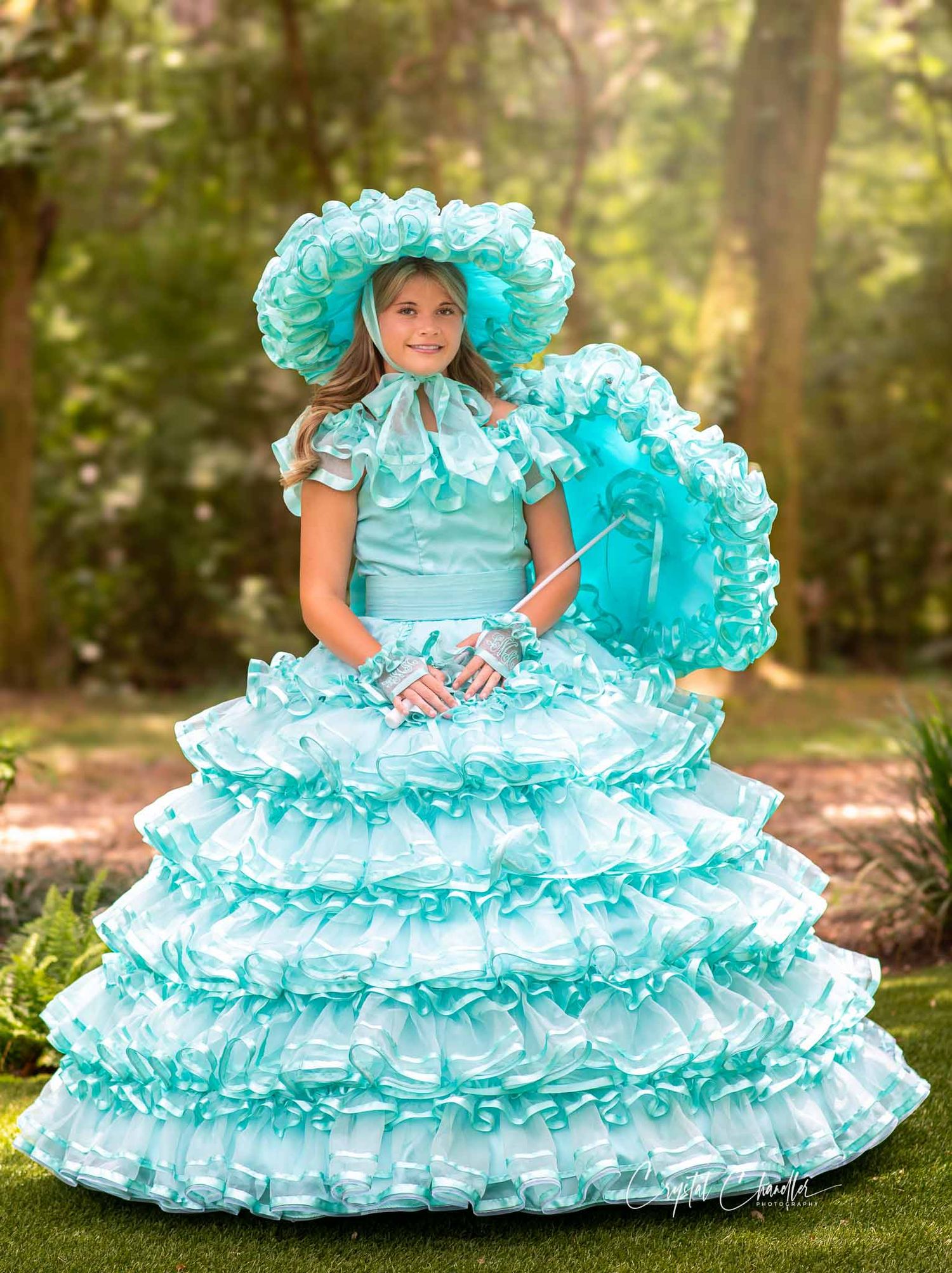 Photograhy, photographer,  person wearing an elaborate turquoise Southern belle costume with ruffles and matching hat in a garden setting.