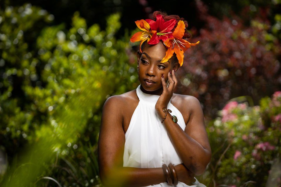Garden portrait with vibrant orange and red floral headpiece and white halter dress.