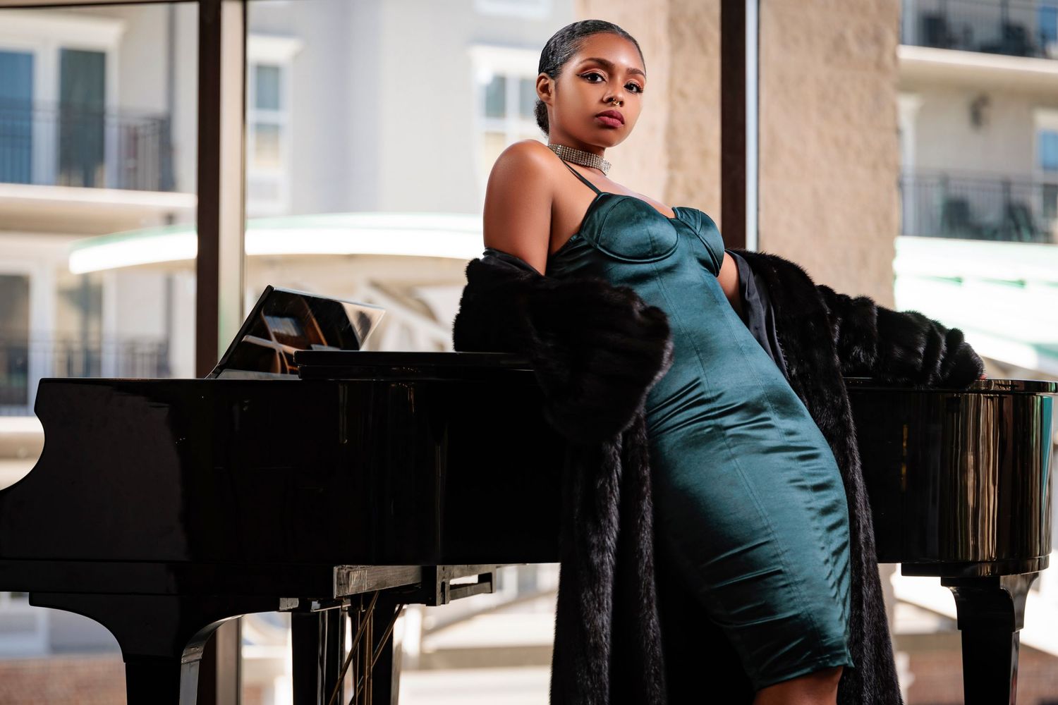Elegant pose in teal evening gown against grand piano backdrop.