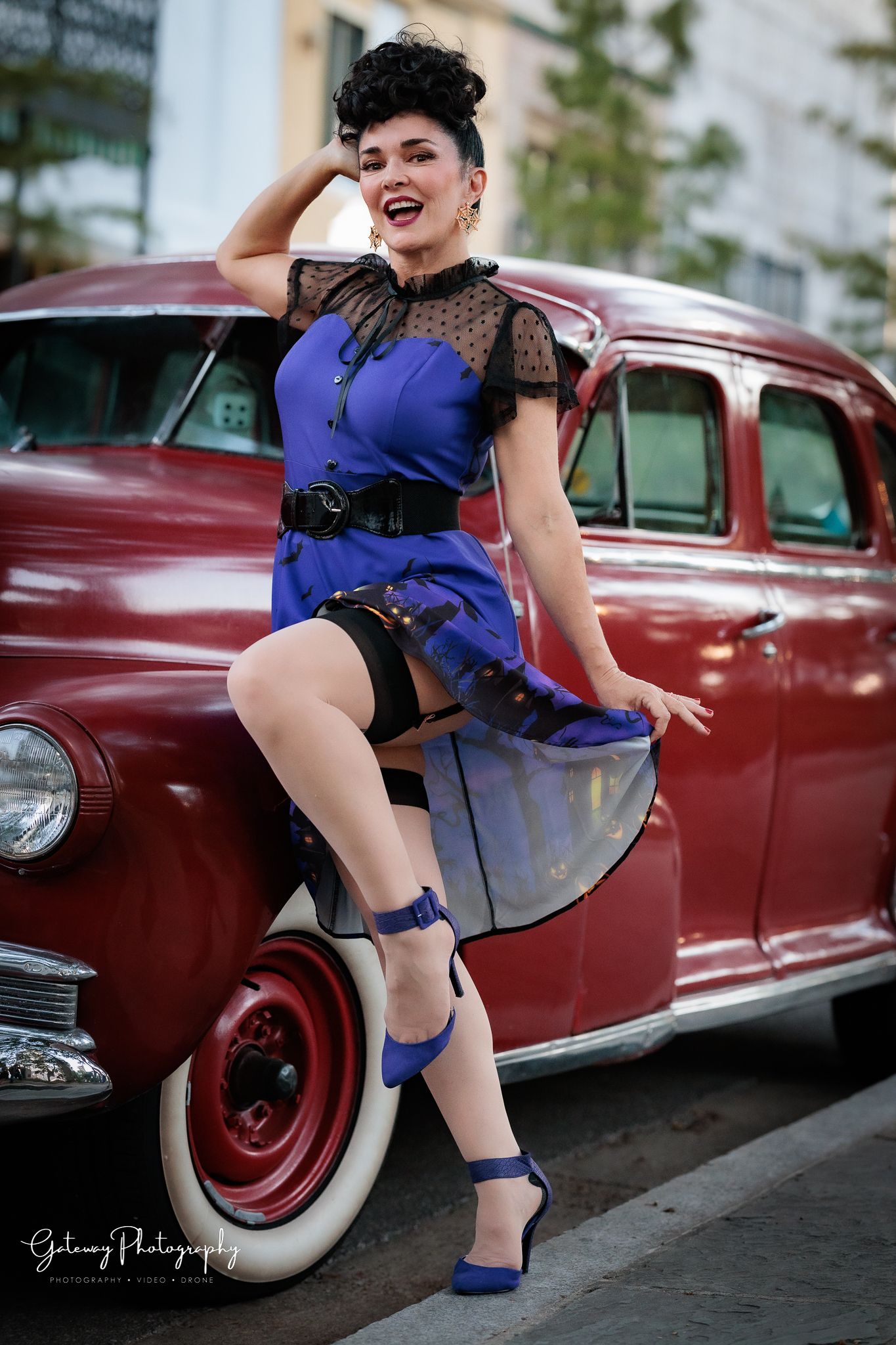 Vintage-style portrait with blue dress and lace details posed against classic red car.