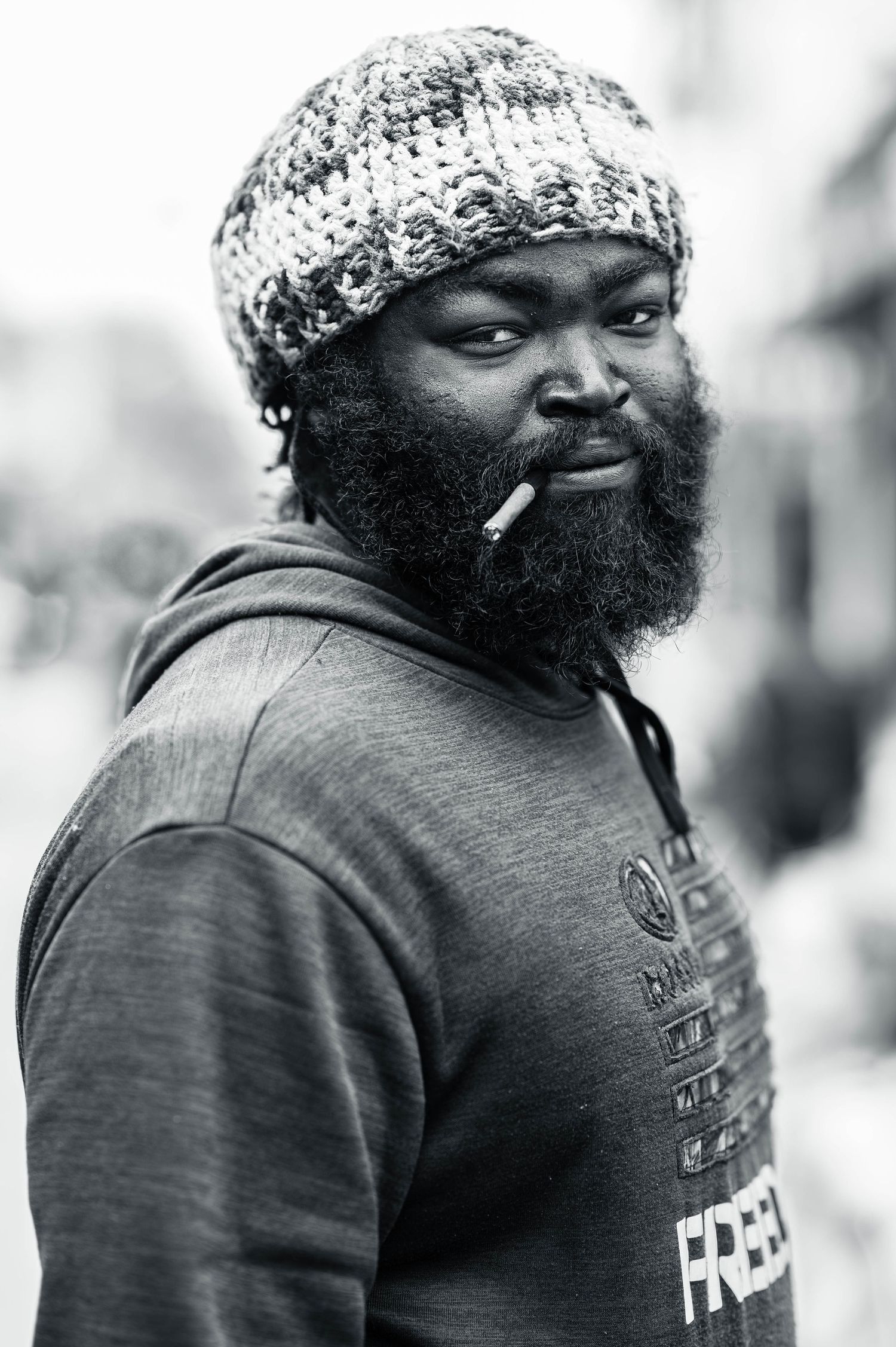 Black and white portrait of a person wearing a knit hat, with a full beard and cigarette, in casual clothing.
