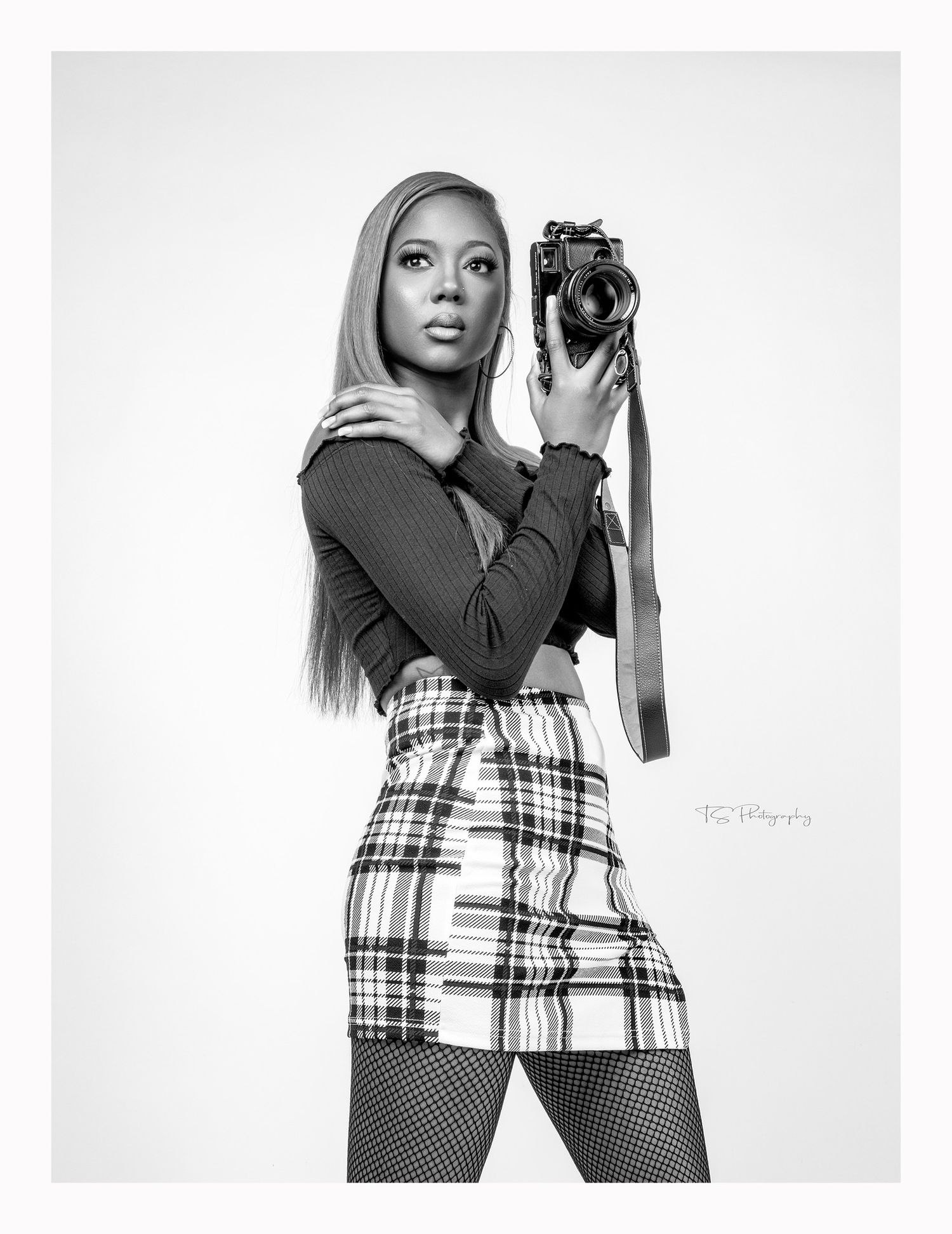 Fashion photo of person holding vintage camera wearing plaid skirt and fishnet stockings.