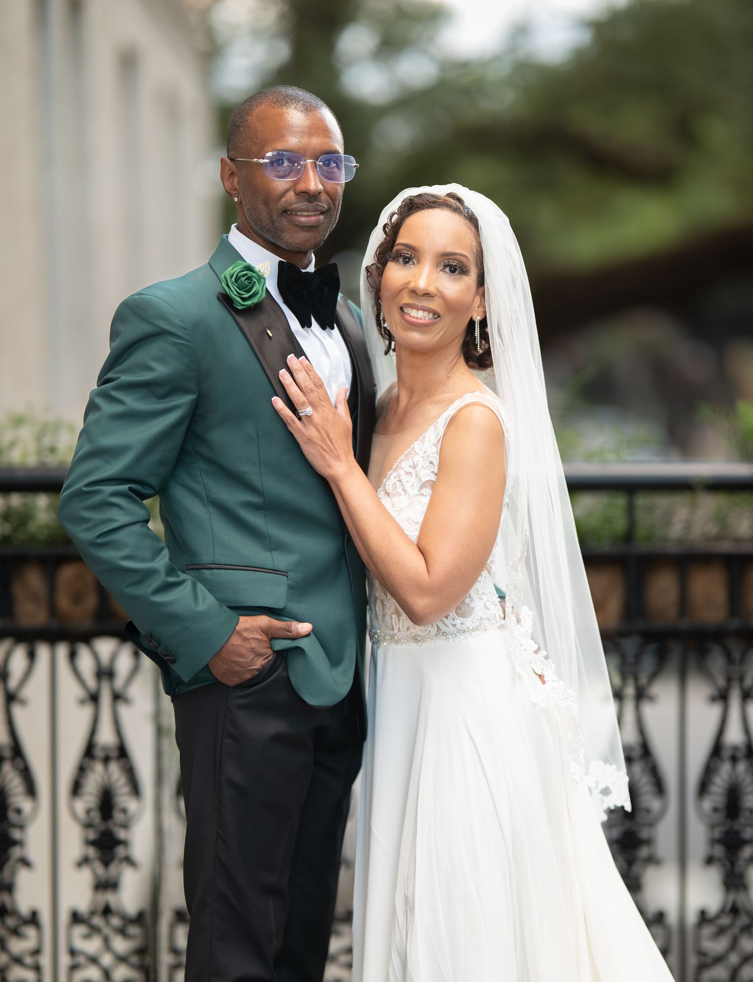 A couple poses together on their wedding day, with the groom in a green suit and bride in a white gown and veil.