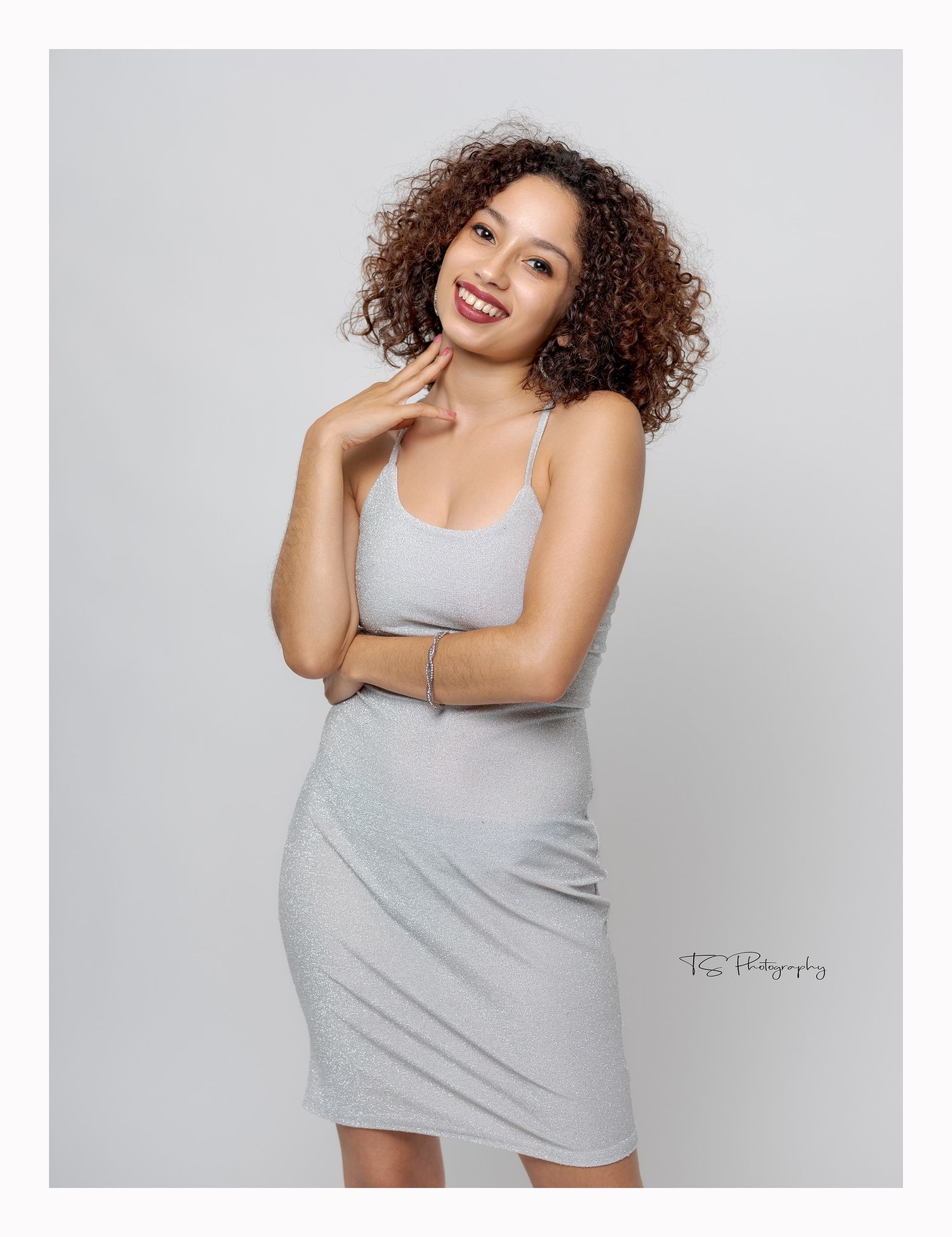 Studio portrait of person in grey dress with curly hair against light background.