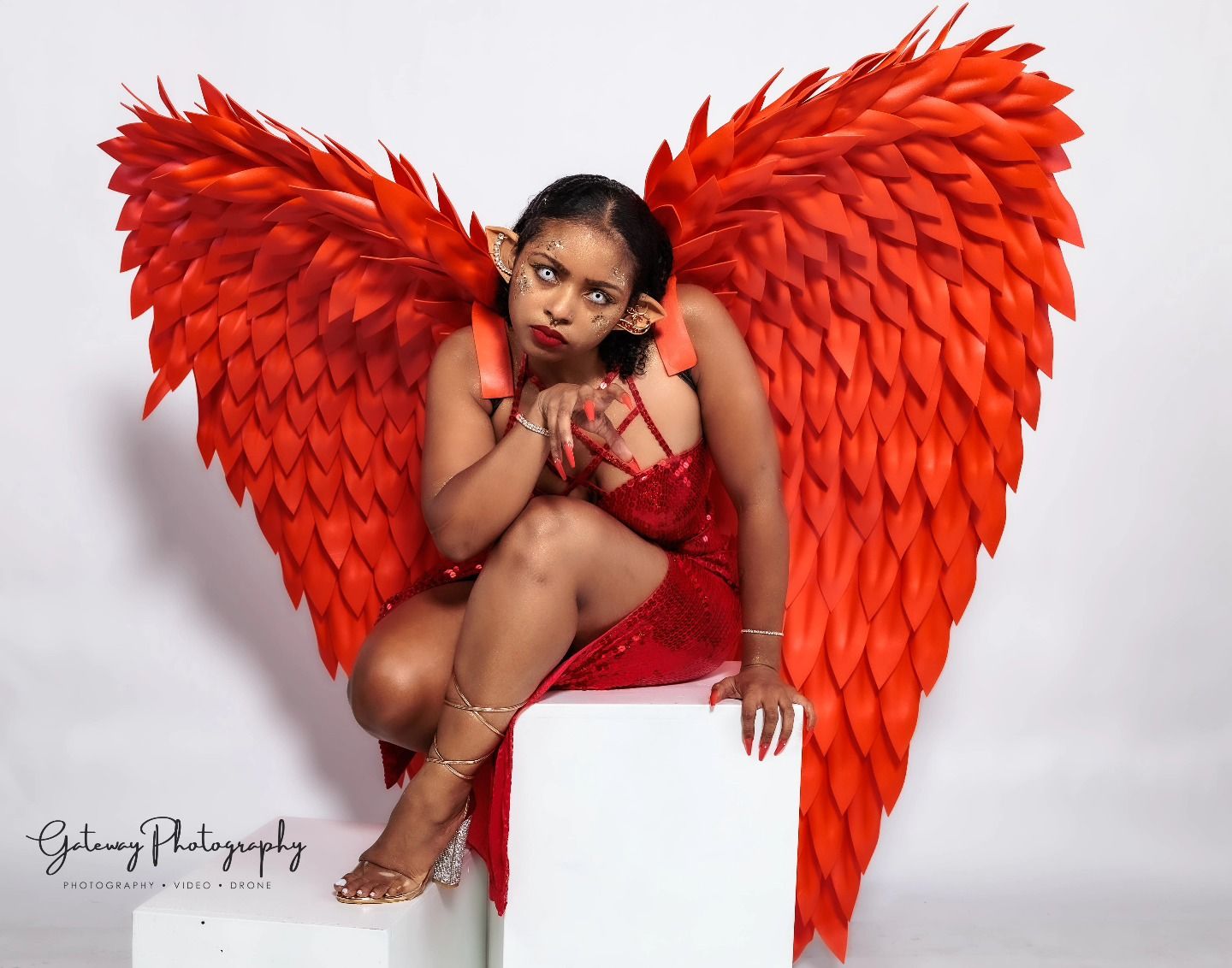 Dramatic studio portrait with large red angel wings and white pedestal.