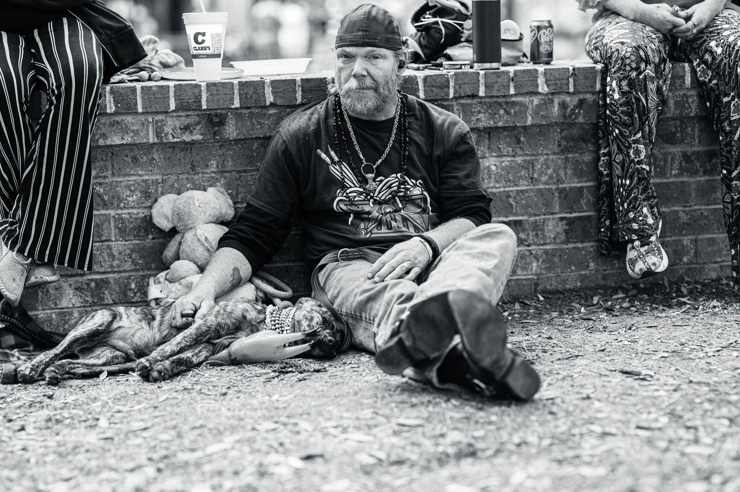 A person sits on the ground against a brick wall wearing casual clothes and a bandana in black and white photography.