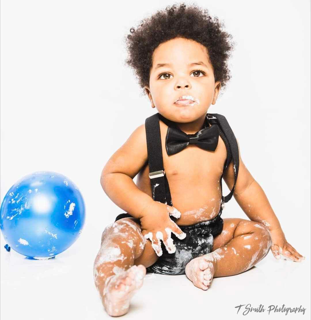 Baby photoshoot with blue balloon and black bow tie on white background.