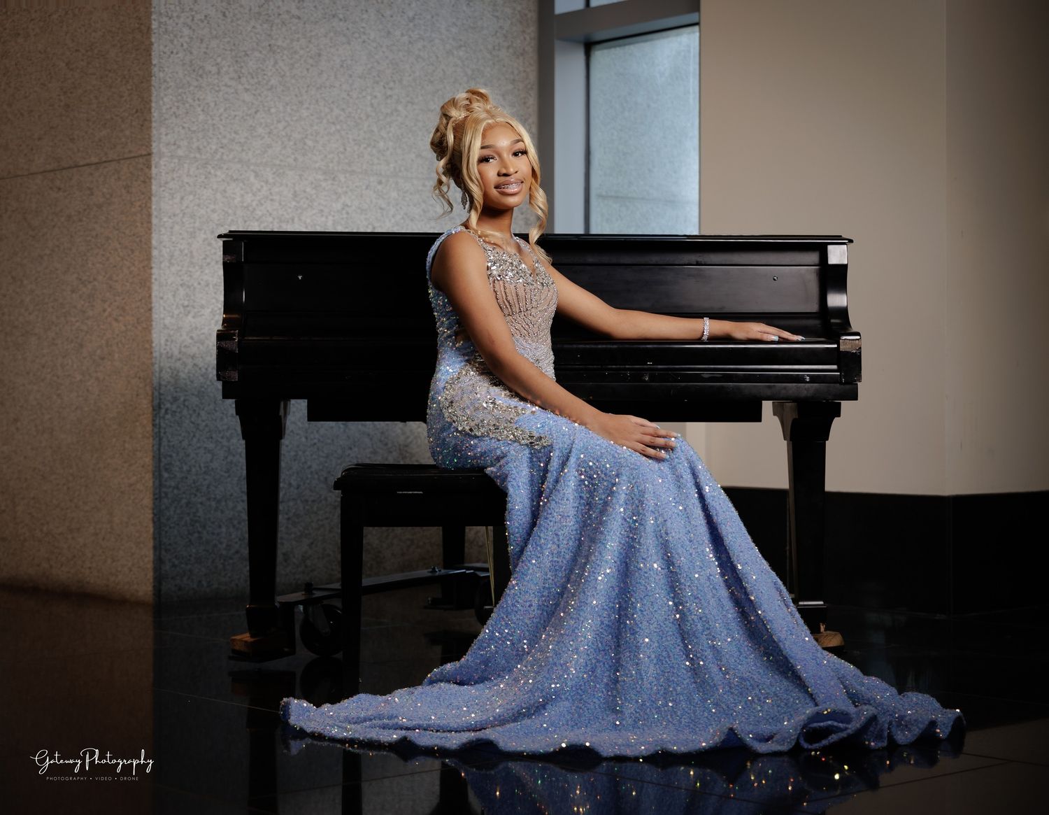 Elegant portrait in blue lace gown seated at grand piano.