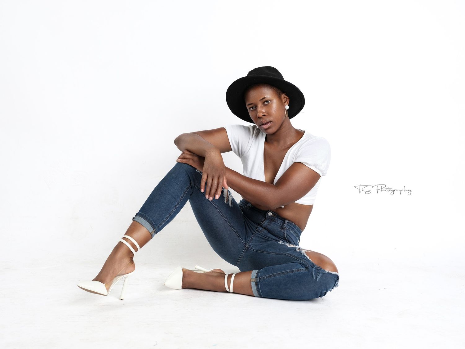 Casual portrait with black hat, white shirt and jeans sitting against white background.