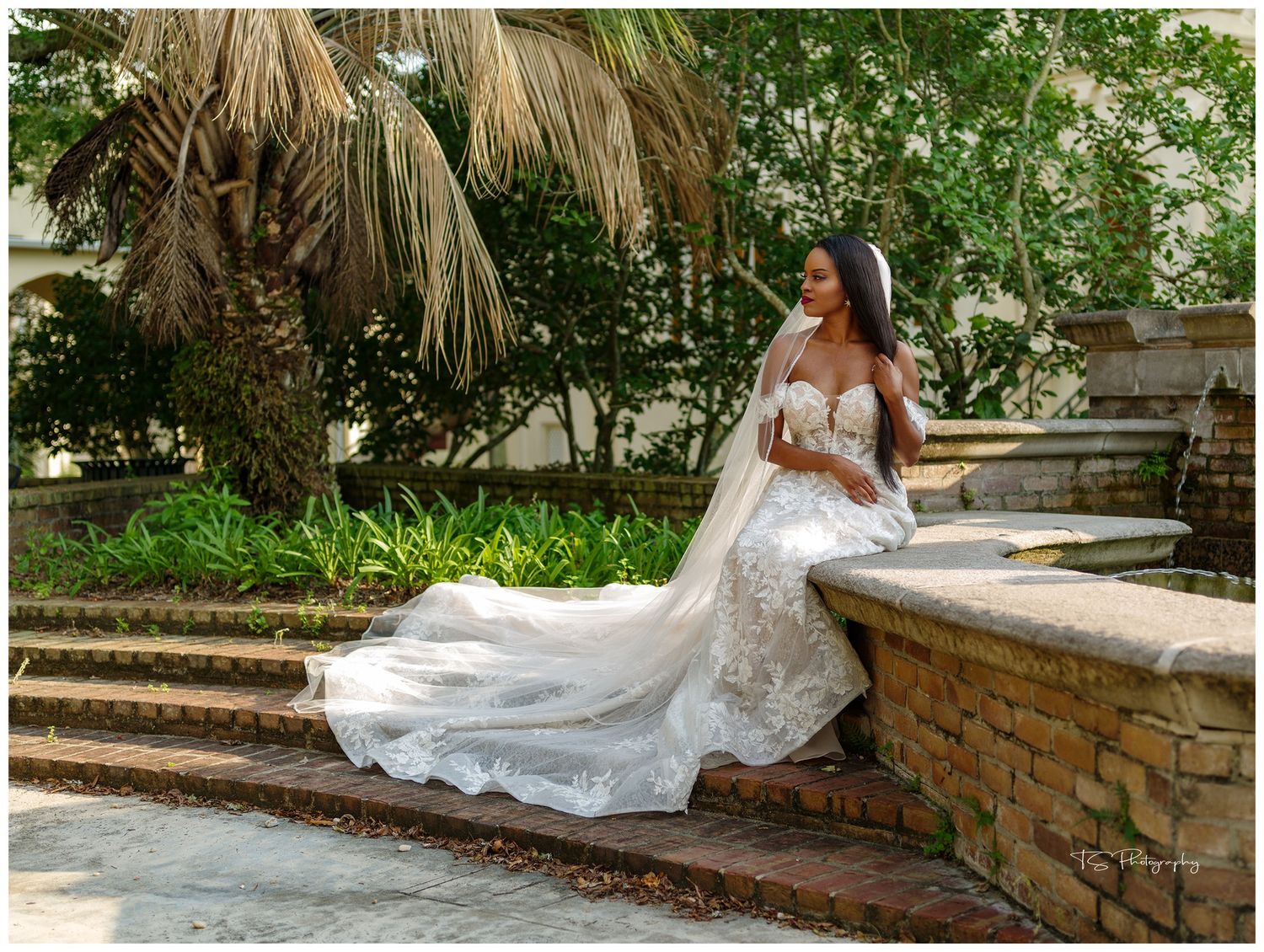 Bridal portrait on stone steps with flowing white lace gown and tropical garden background.