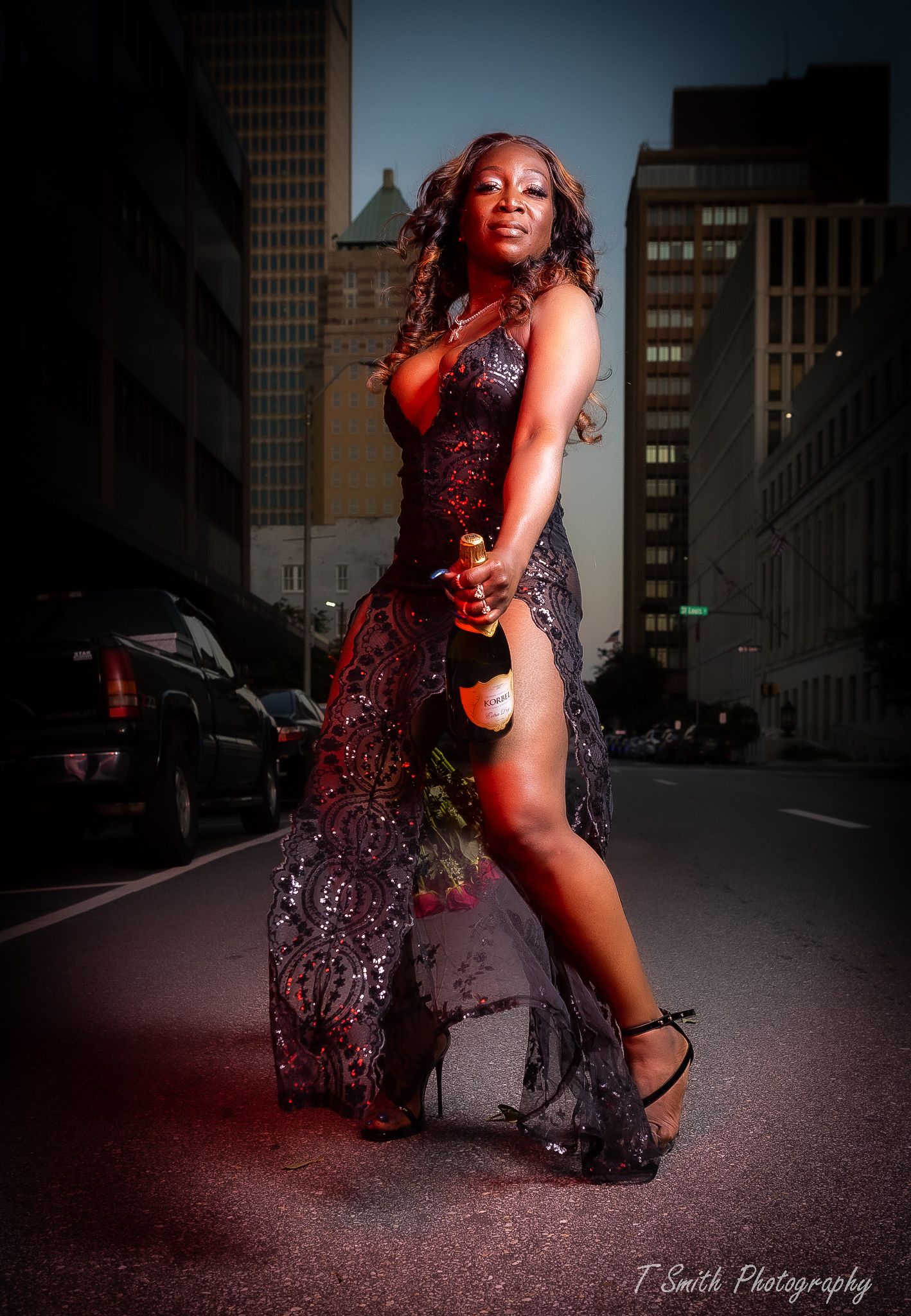 Dramatic urban fashion photo of woman in sparkly dress posing on city street at dusk.