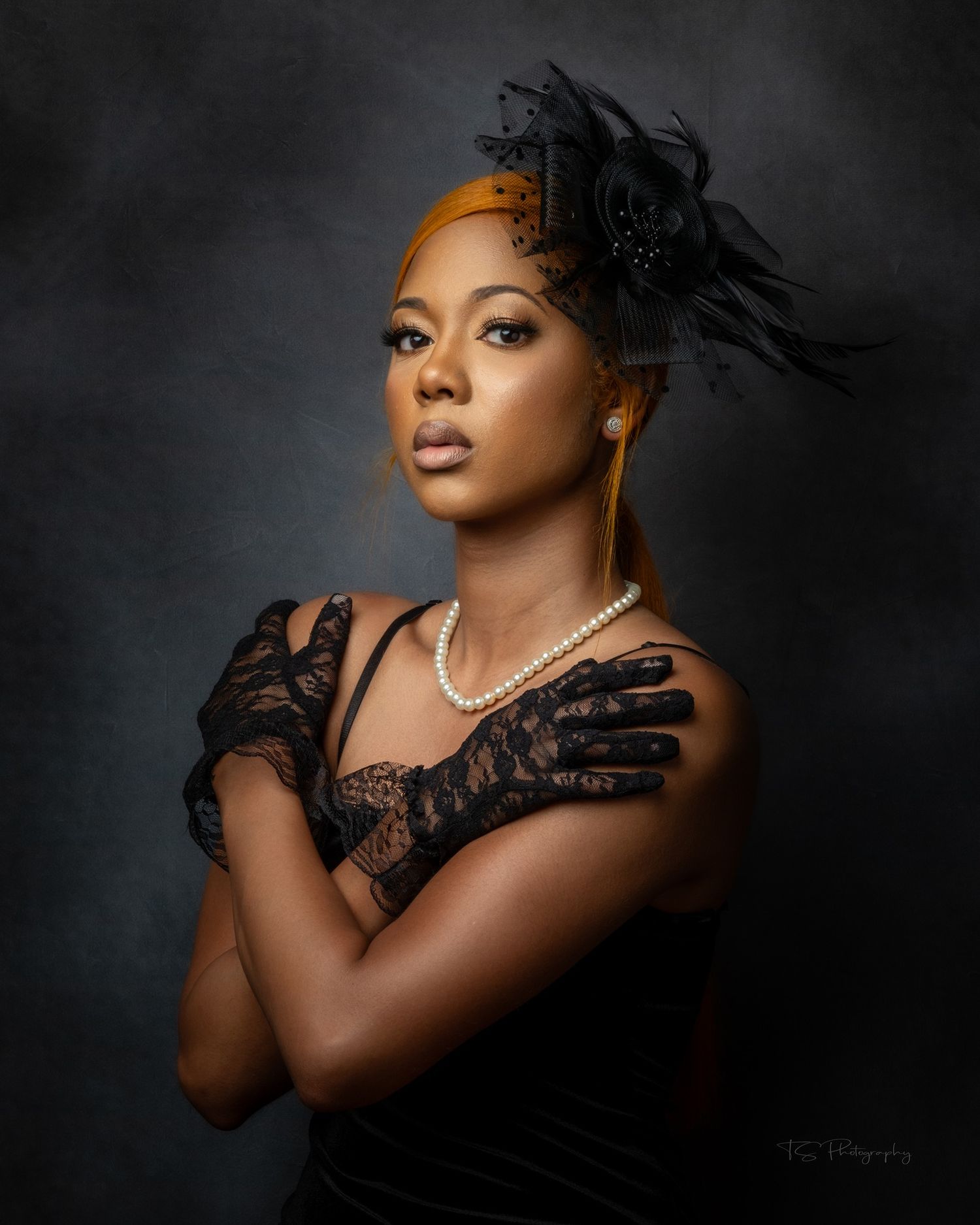 Dramatic portrait with black lace gloves and pearl necklace against dark background.