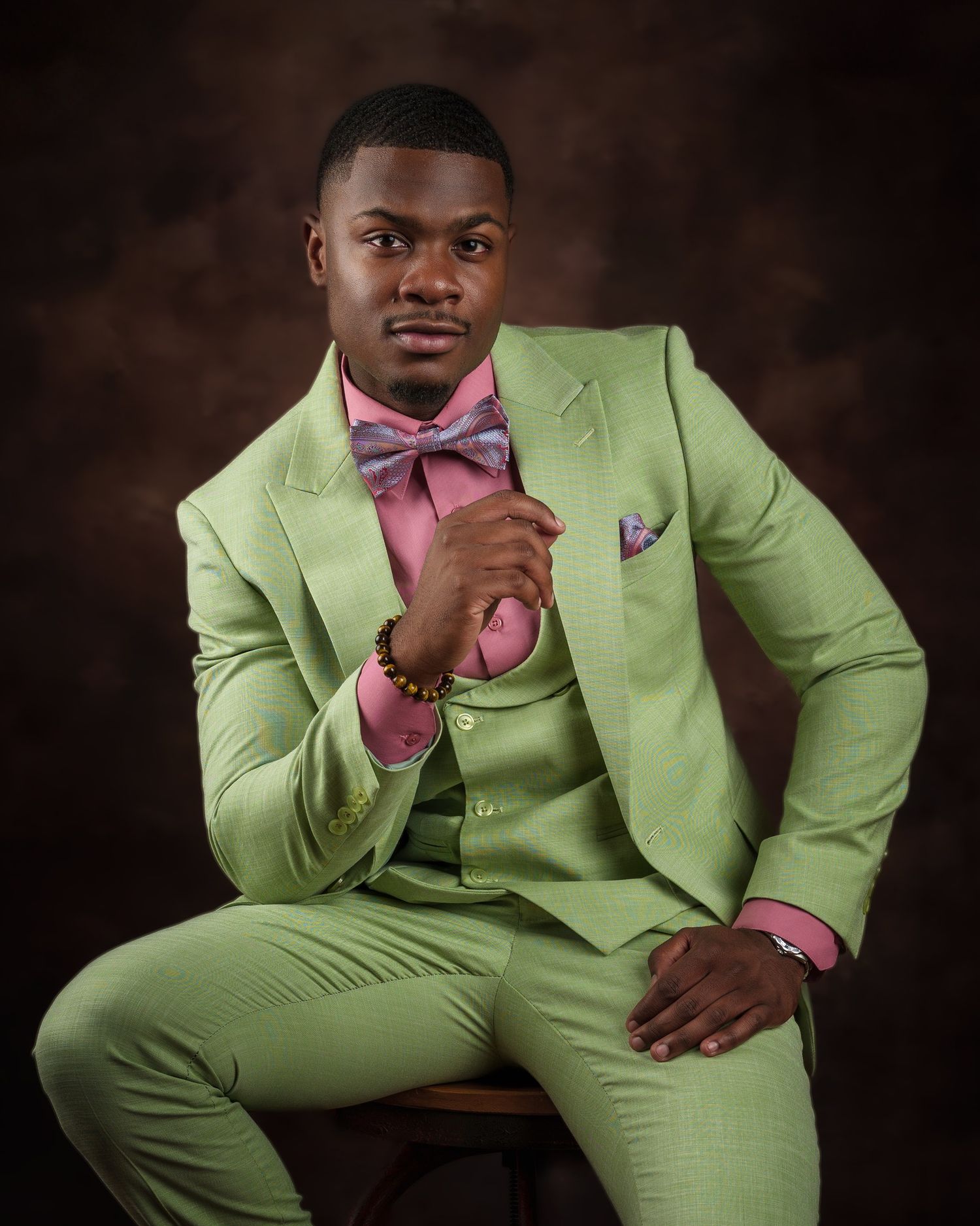 Professional portrait of person wearing lime green suit with pink bowtie against dark background.