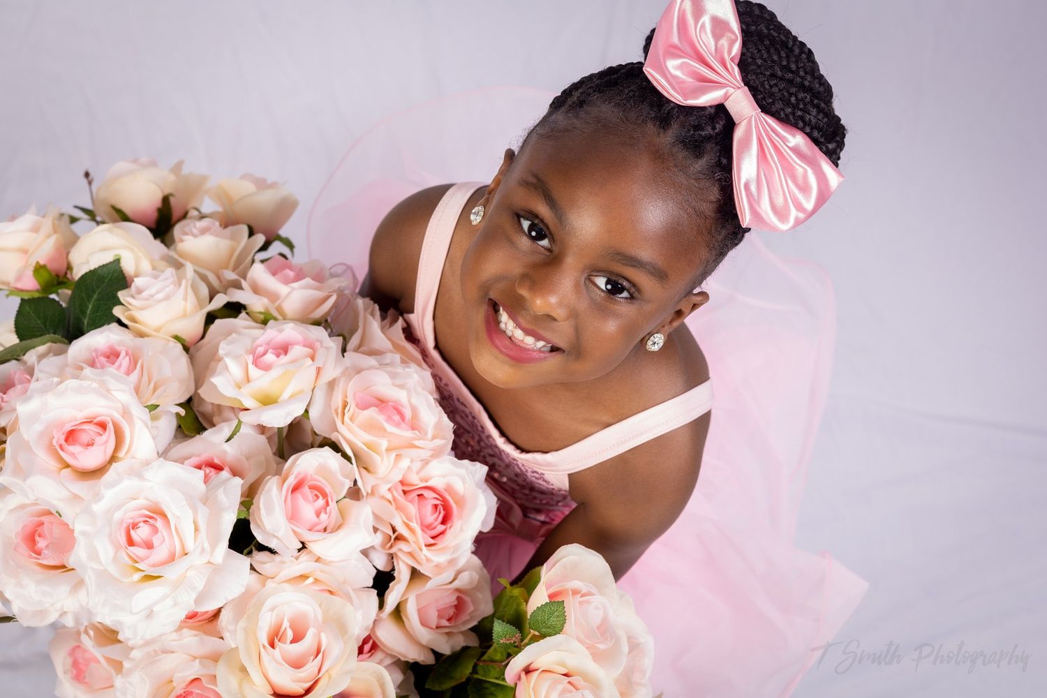 A portrait with pink roses featuring a pink bow and tulle dress.
