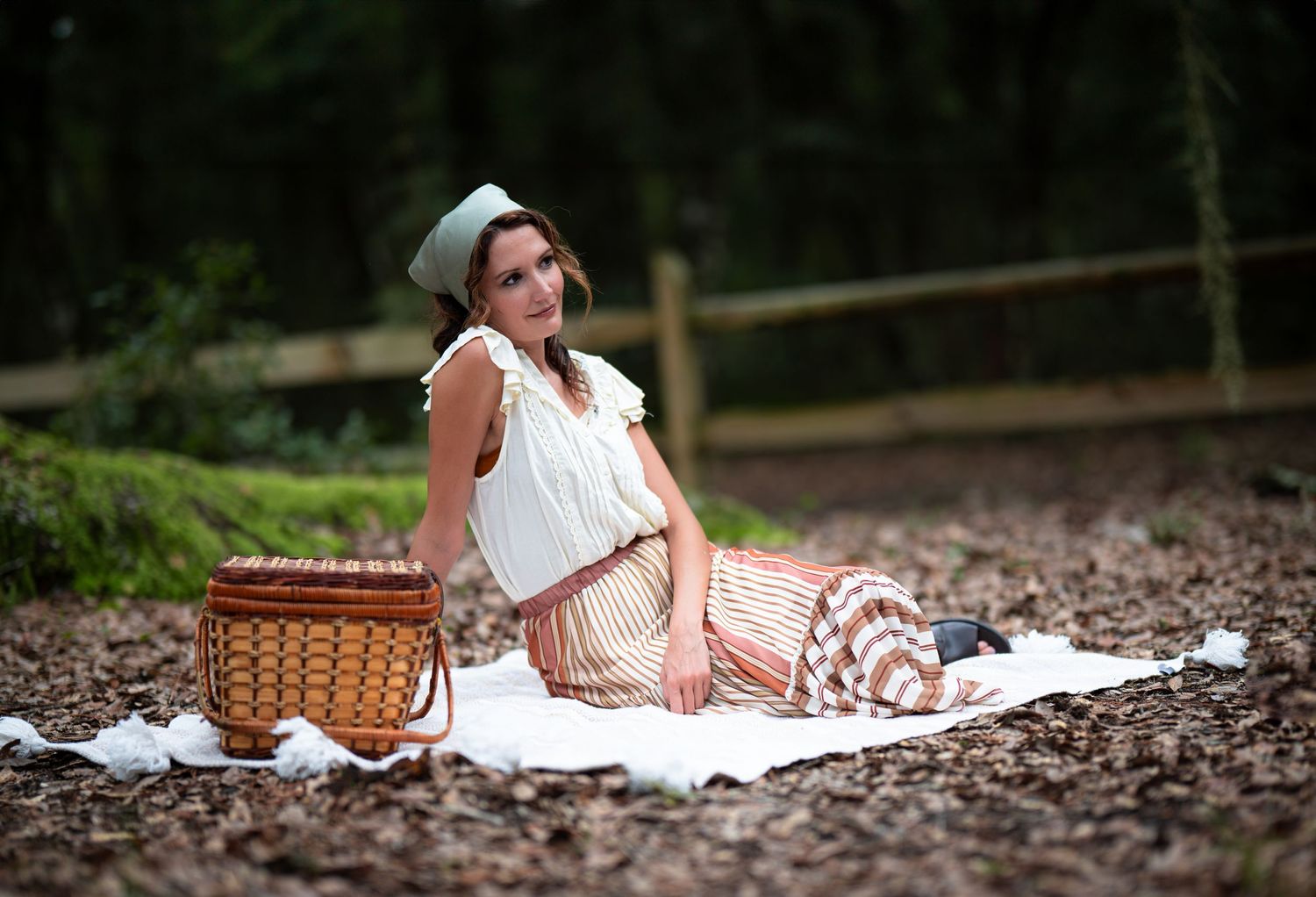 Vintage-inspired picnic scene with a wicker basket and white blanket on forest ground.