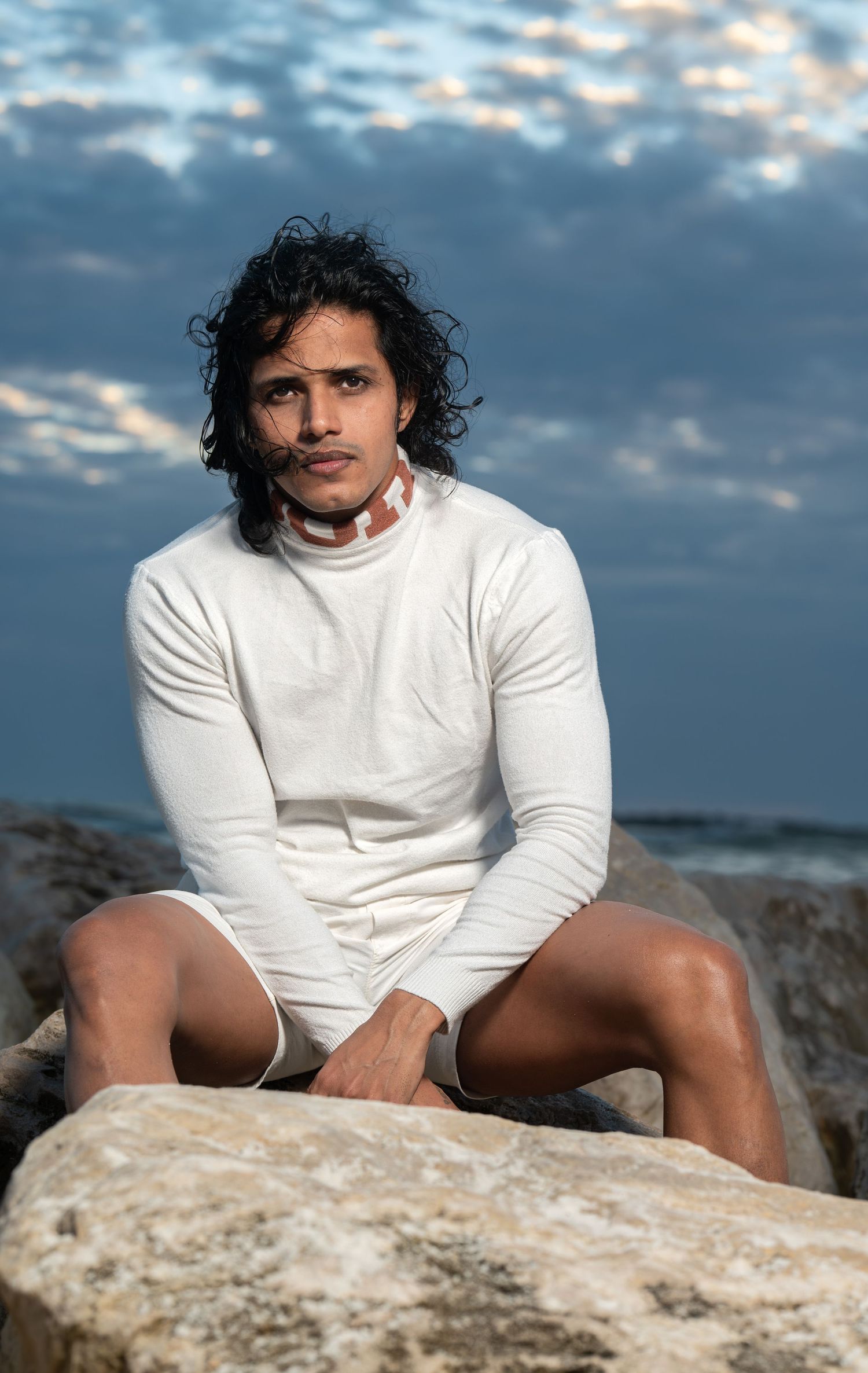 Beachside portrait at sunset featuring an all-white outfit against dramatic cloudy sky.