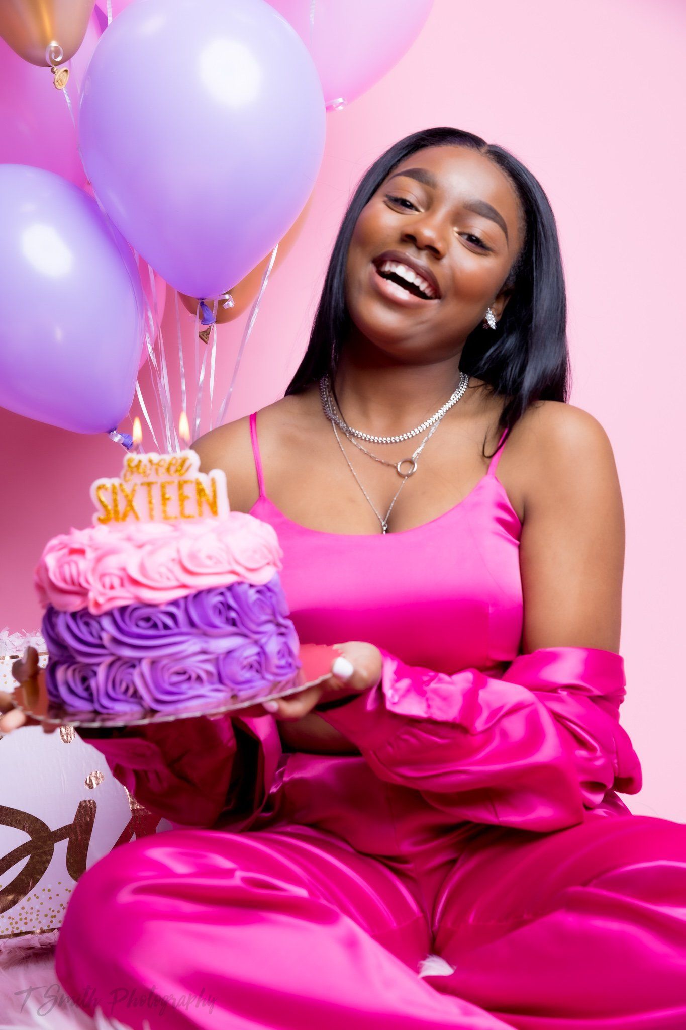 Birthday celebration with pink and purple balloons surrounding a beautifully decorated two-tier cake in matching colors.