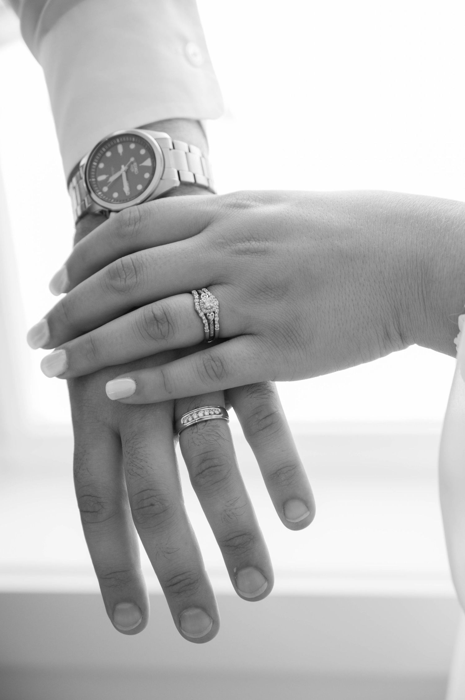 Black and white photo showing two hands with wedding rings and a watch, symbolizing marriage and commitment.