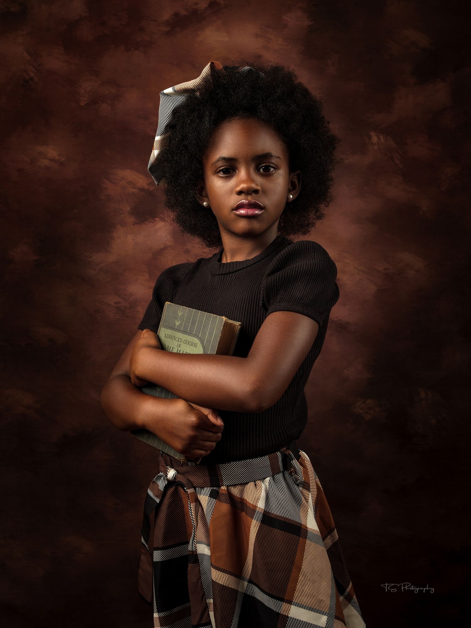 Studio portrait of young student holding book wearing plaid skirt against dark background.