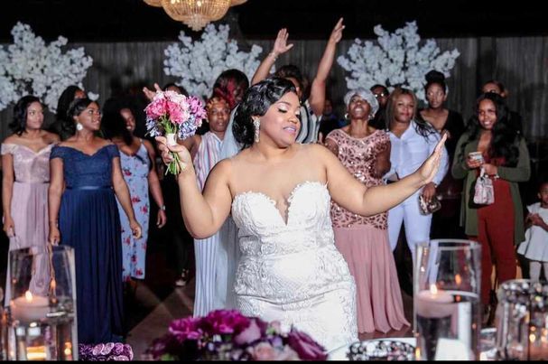 A joyful wedding reception scene with a bride in white celebrating at a decorated table with guests.