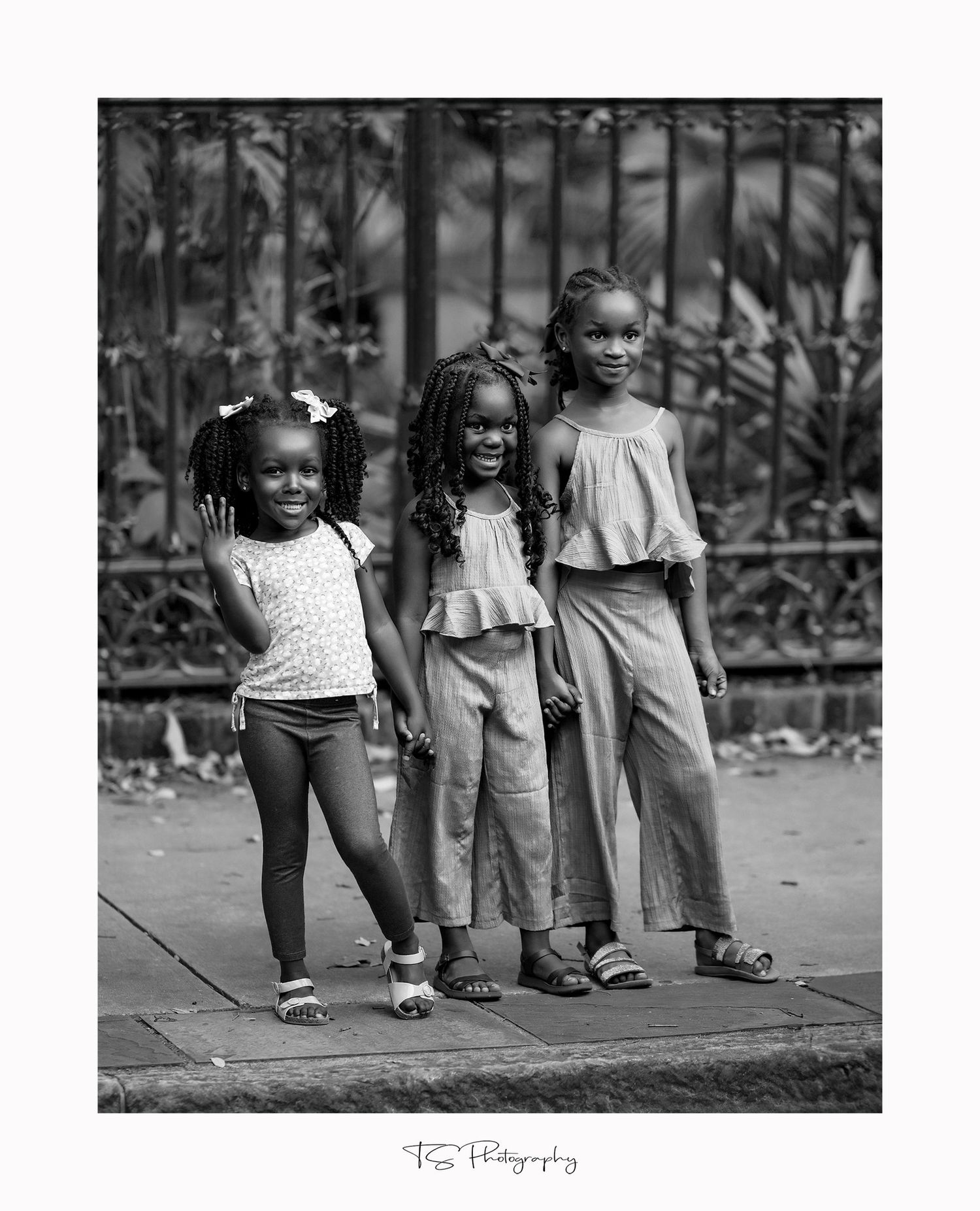 Black and white portrait of three children posing together on sidewalk.