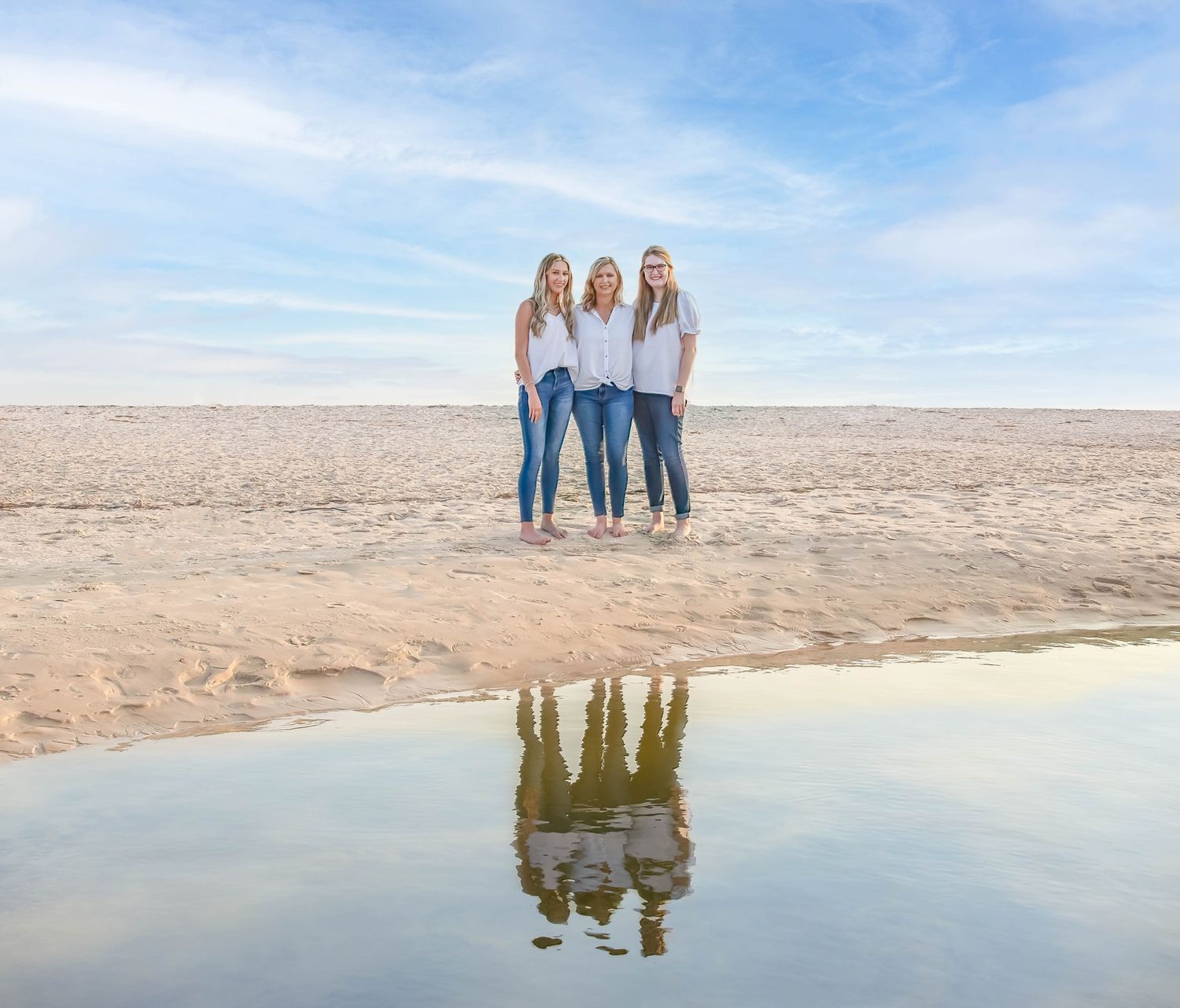 Photograhy, photographer, Mobile, AL Three people in matching white tops and jeans standing on beach with reflection in water.
