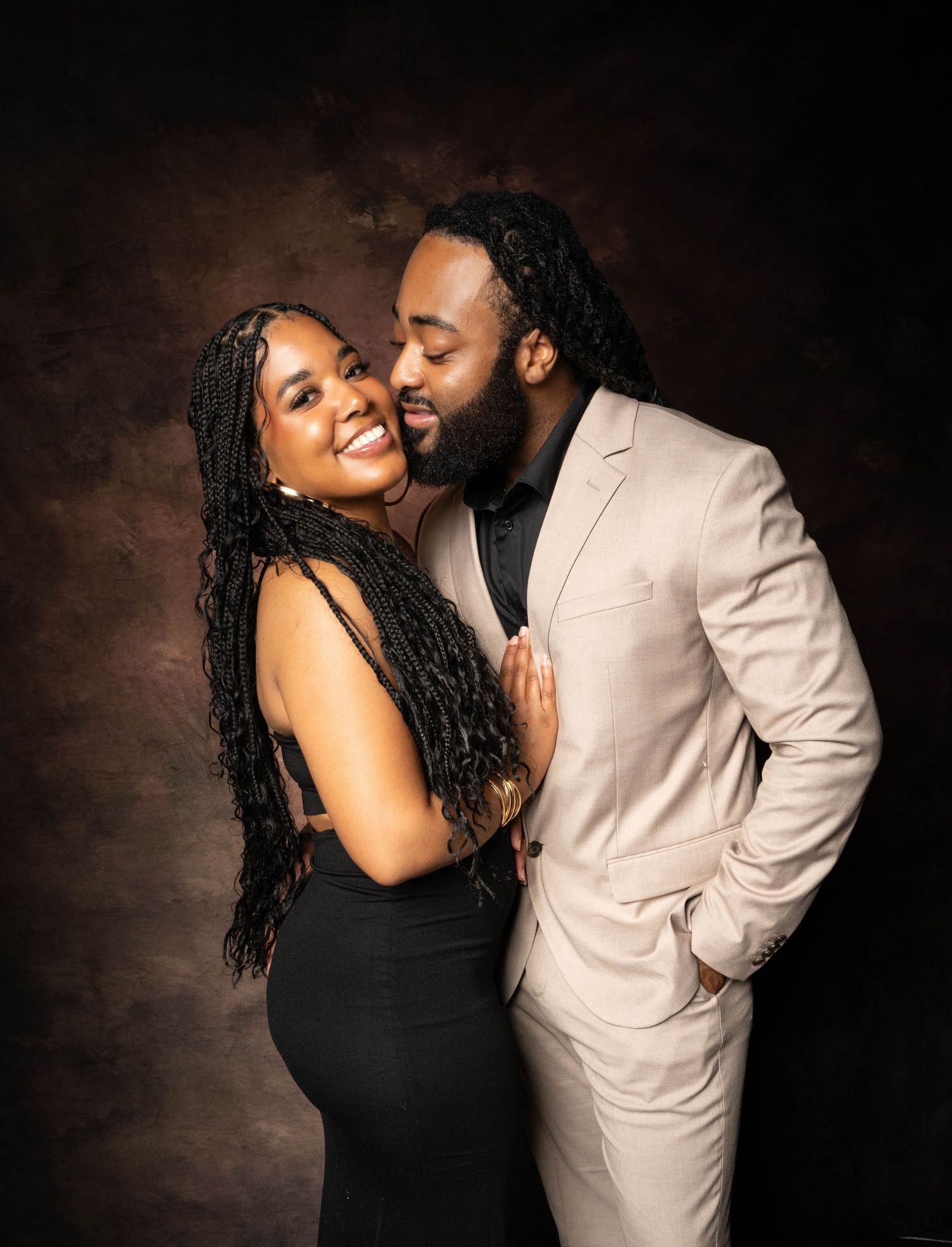 A romantic couple poses intimately in contrasting black and cream outfits against a dark textured background.