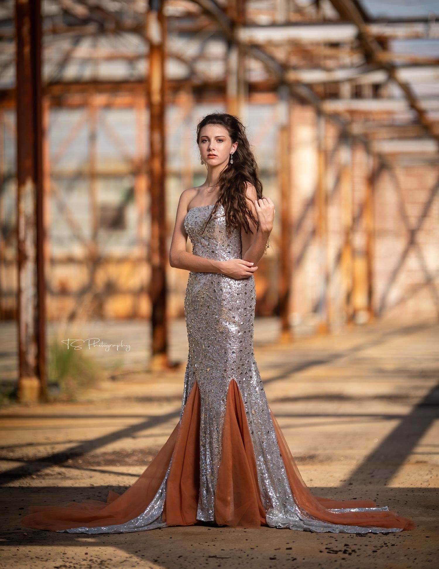 Sparkling silver sequin evening gown with dramatic side slits photographed against industrial rustic backdrop at sunset.