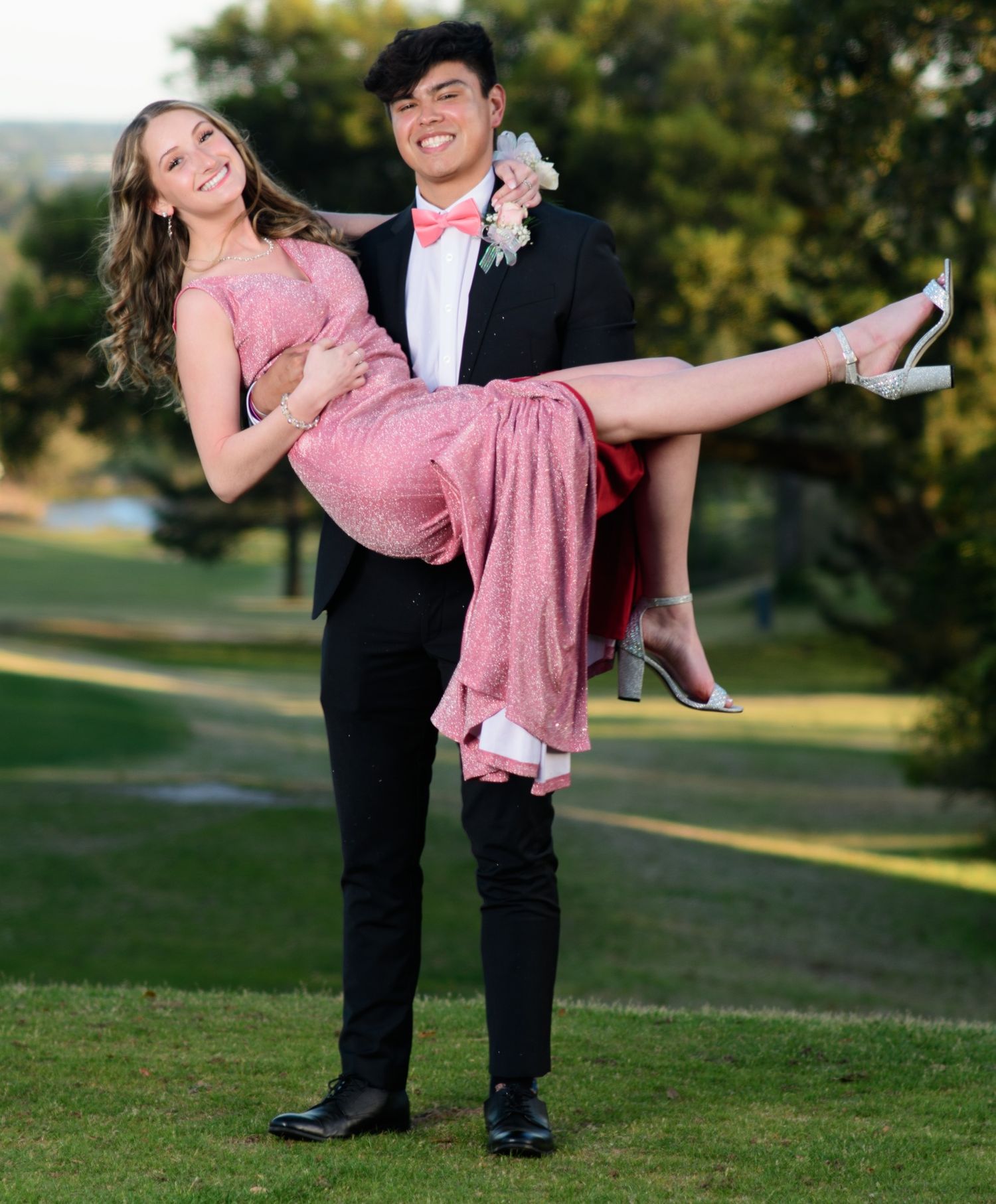 Couple in formal attire posing playfully on grass during outdoor photoshoot.
