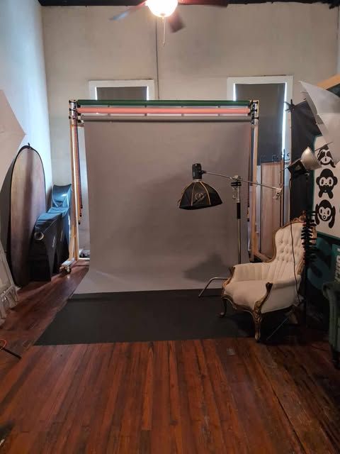 Photography studio setup with gray backdrop, lighting equipment, vintage chair, and hardwood floors in a professional space.