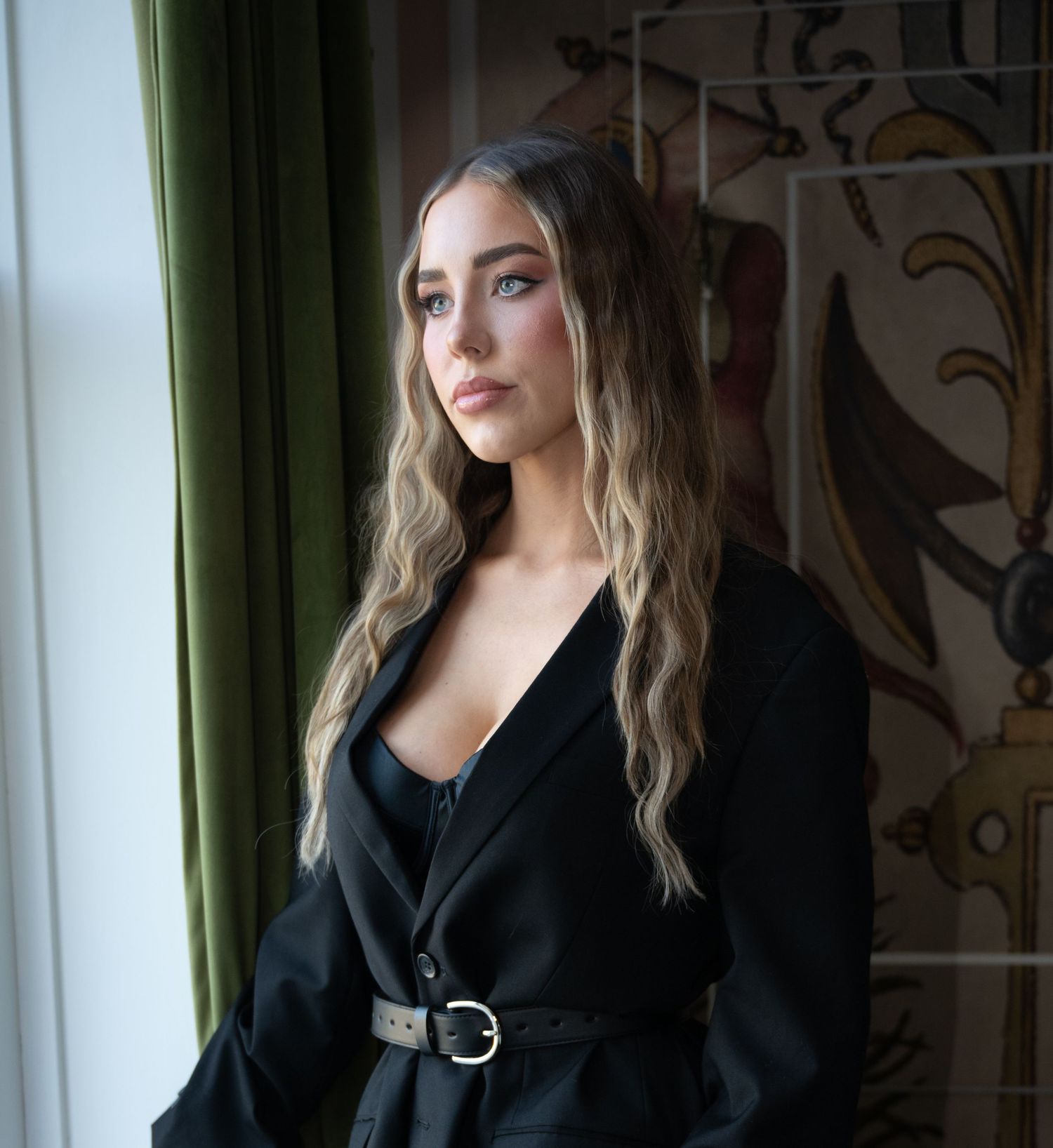 Person in black attire poses near window with natural light creating moody artistic portrait.