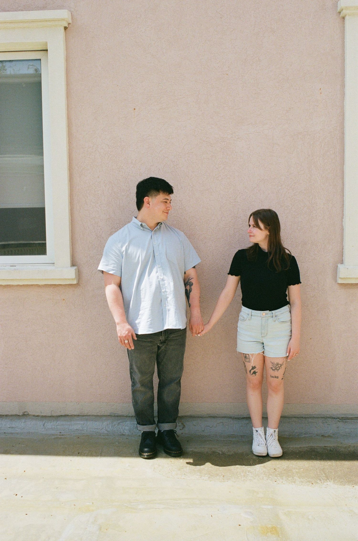 Two people lean against a beige wall with windows in a minimalist triptych photo series.