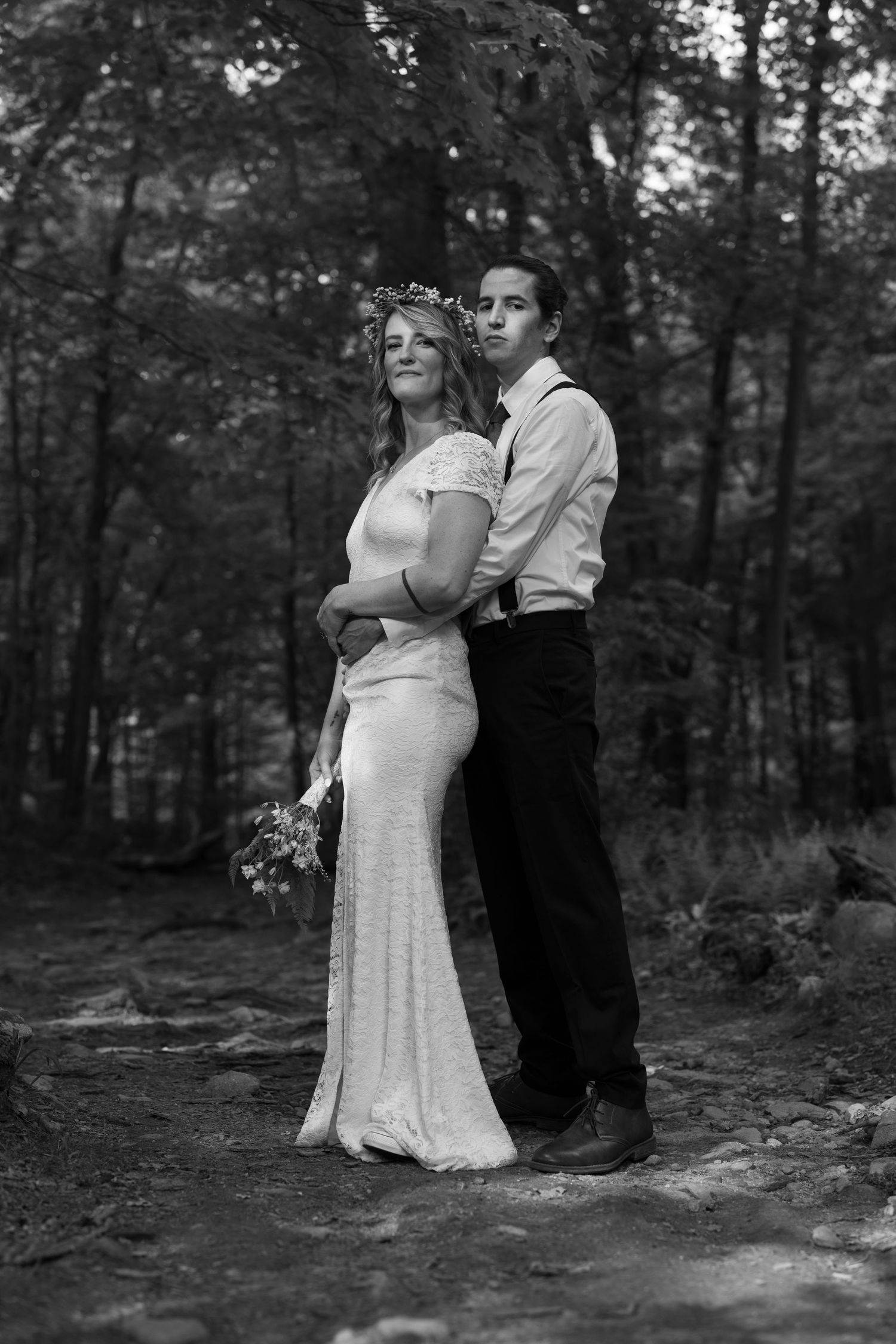 A romantic black and white wedding photo of a couple embracing in a forest setting.