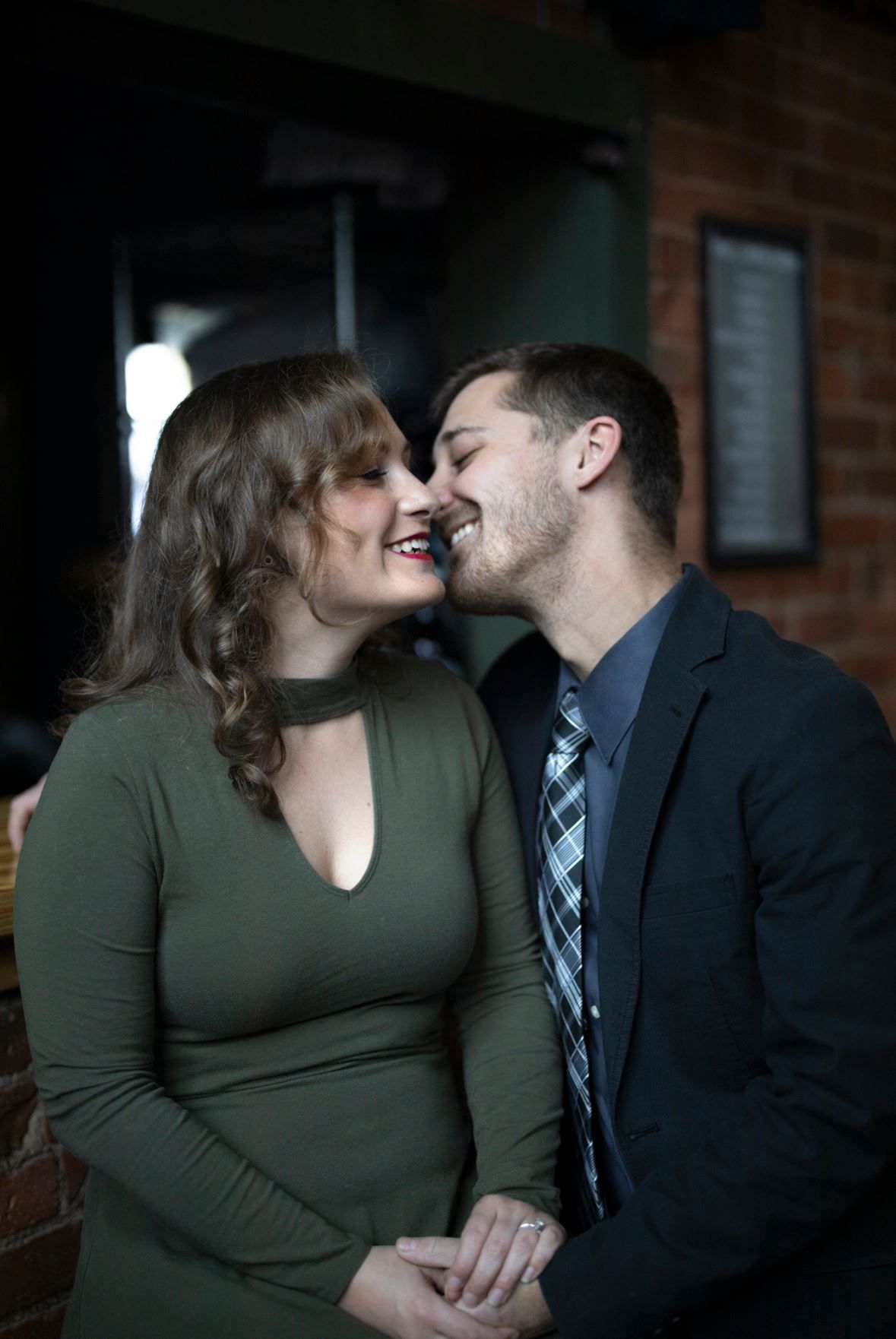A tender moment between a couple in a dark venue, with the woman in olive green and the man in a blue tie and suit.